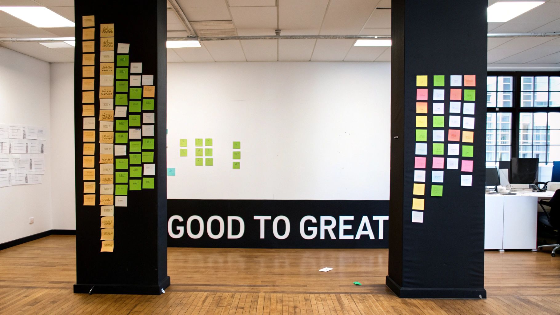 An office space featuring two black pillars covered in colorful sticky notes, with 'GOOD TO GREAT' on a wall.