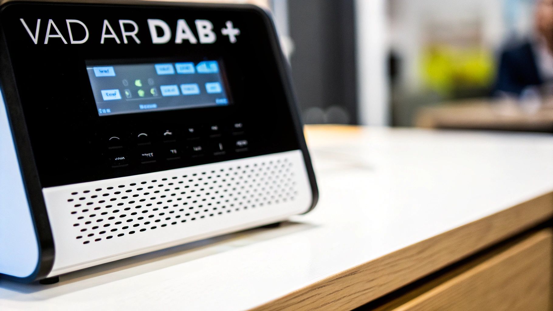 En svart och vit digitalradio med texten 'VAD ÄR DAB+' på en vit och träfärgad bänk.