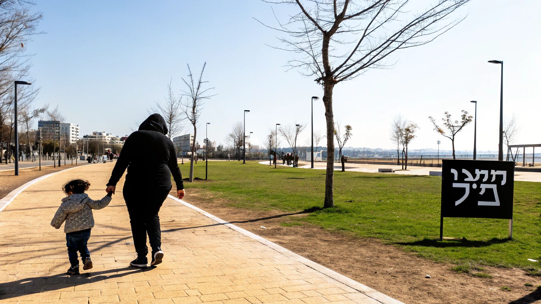 אם והילד שלה מטיילים יחד בפארק עירוני ביום בהיר, מחזיקים ידיים בדרך המרוצפת