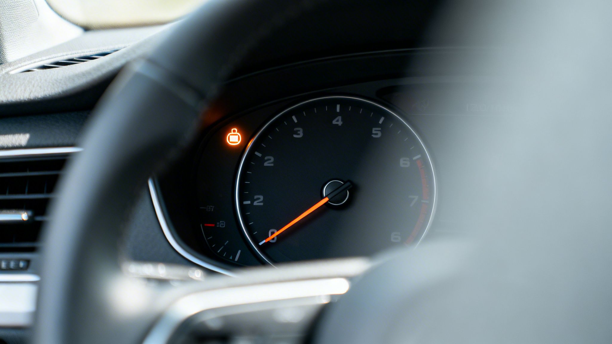 Close-up of a car dashboard showing an illuminated orange engine warning light on the instrument cluster.
