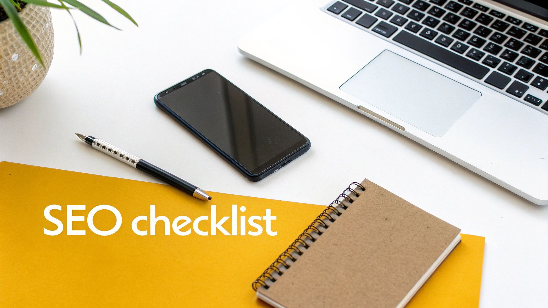 Desk flat lay showing a laptop, phone, pen, and 'SEO checklist' on yellow paper, ideal for optimization tasks.