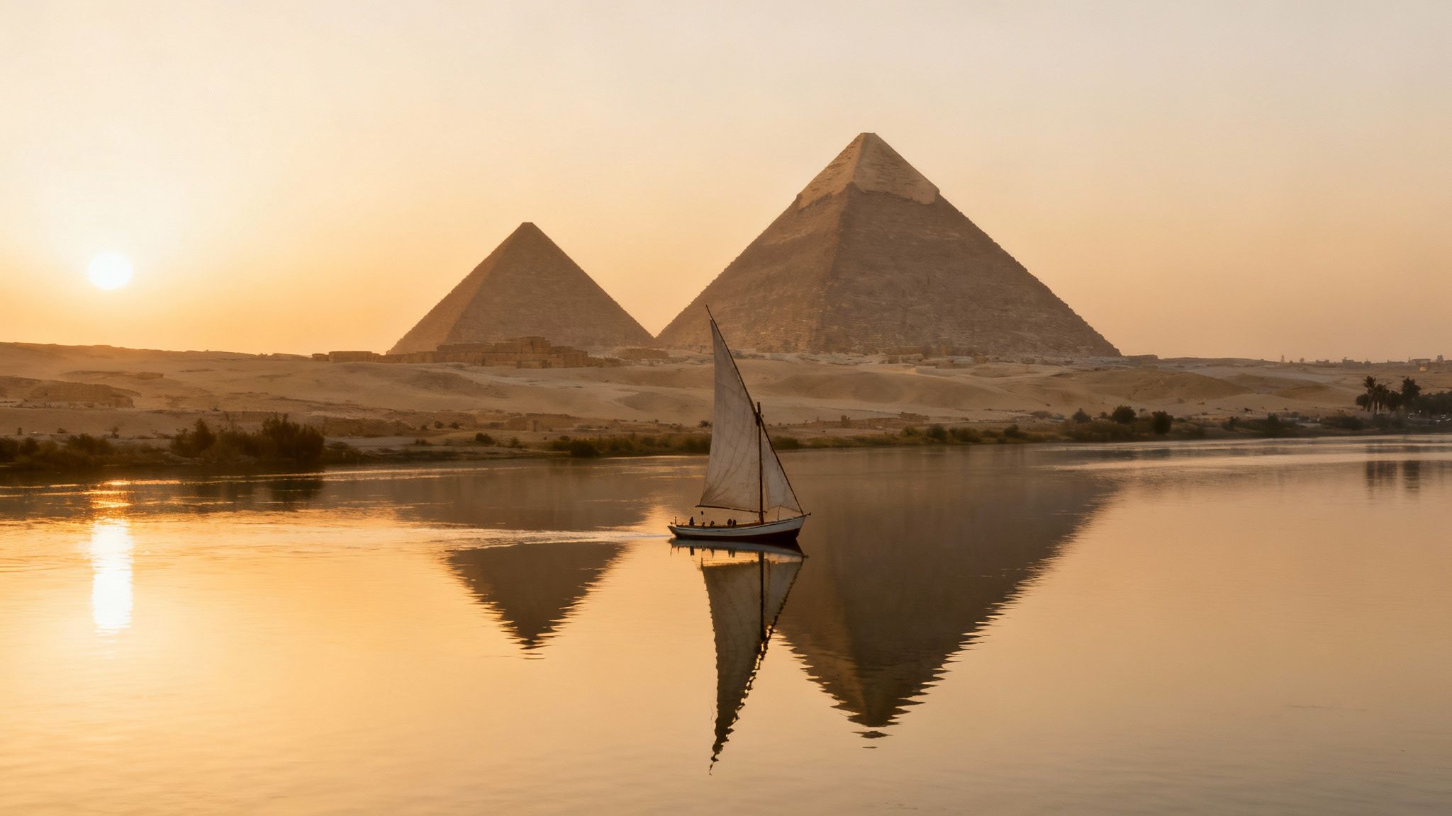 A felucca sails on the Nile River at golden sunset with the majestic Giza Pyramids.
