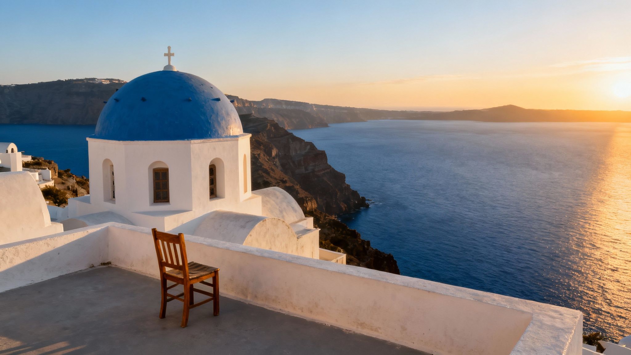 A white church with a blue dome in Santorini, Greece, at sunset overlooking the Aegean Sea.