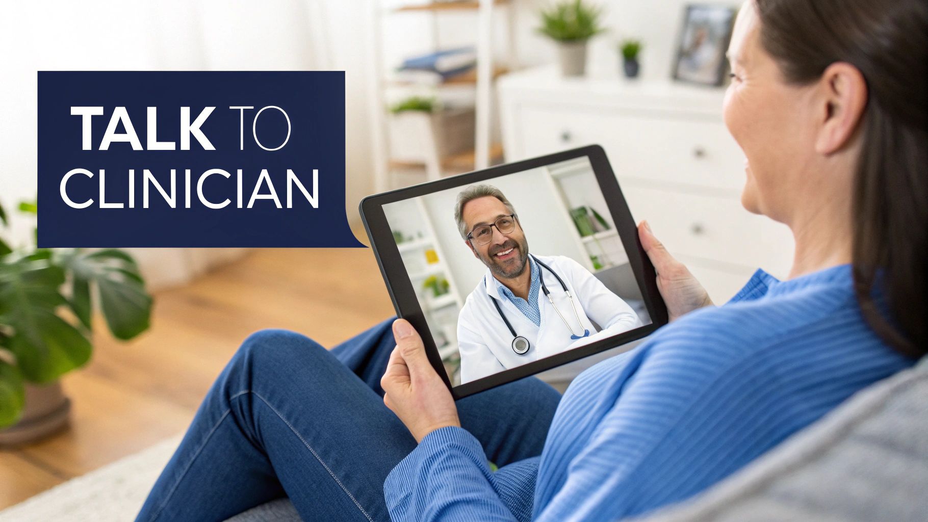 Smiling woman on a couch having a telehealth video call with a male doctor on a tablet.