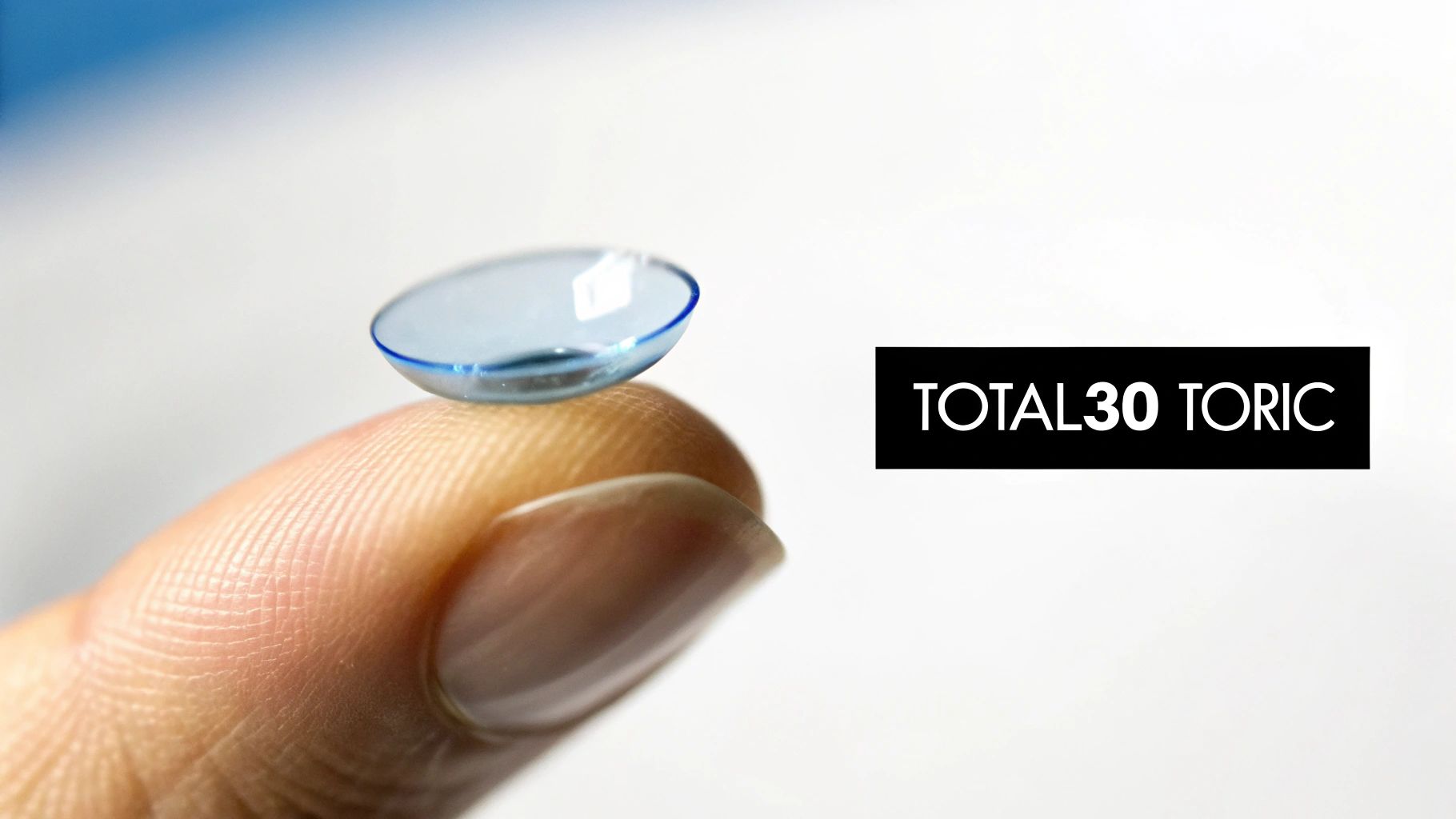 A blue TOTAL30 TORIC contact lens rests on a fingertip against a white background.