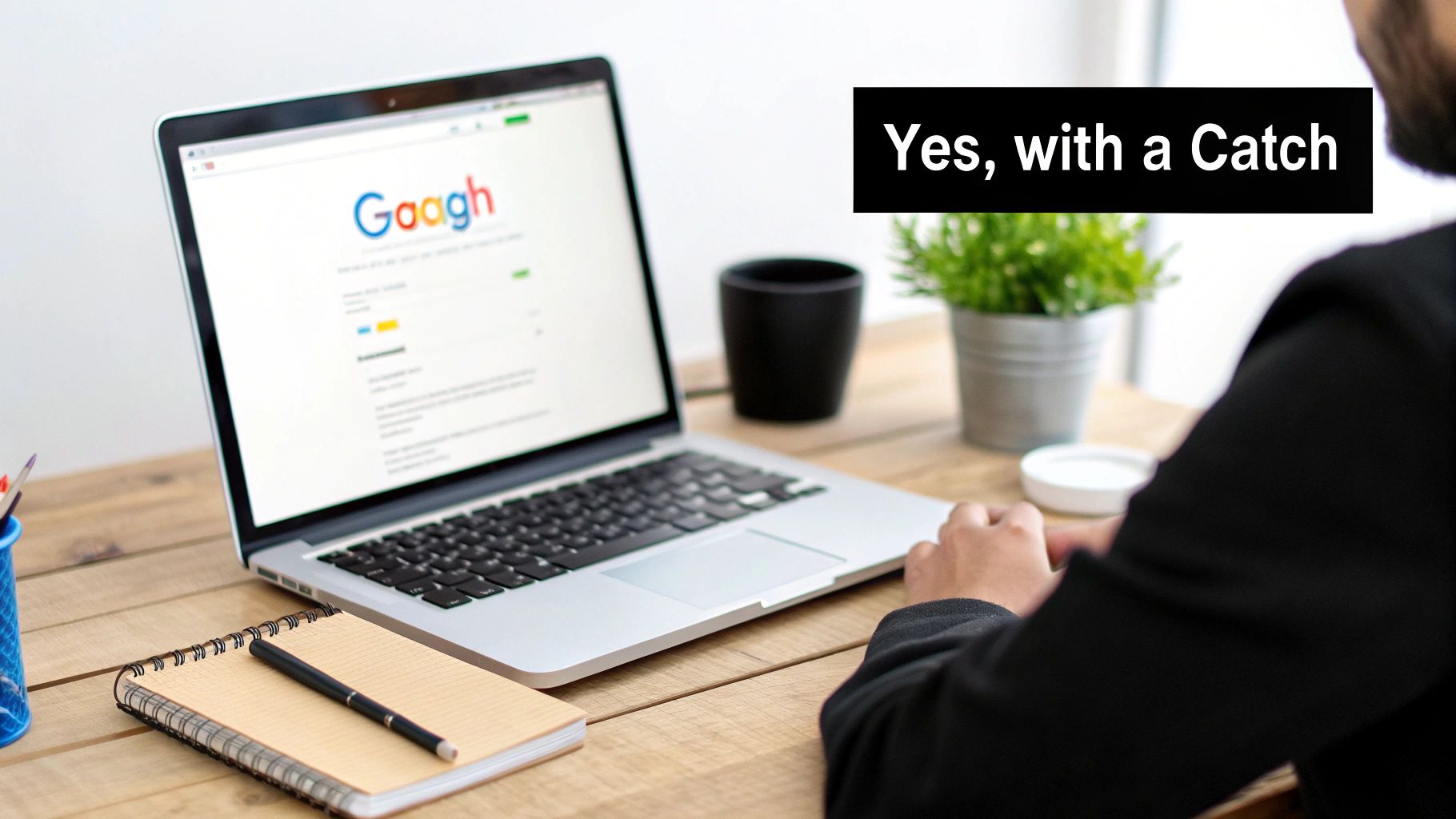 A person at a wooden desk, working on a laptop displaying 'Gaagh' search, with a notebook and pen.