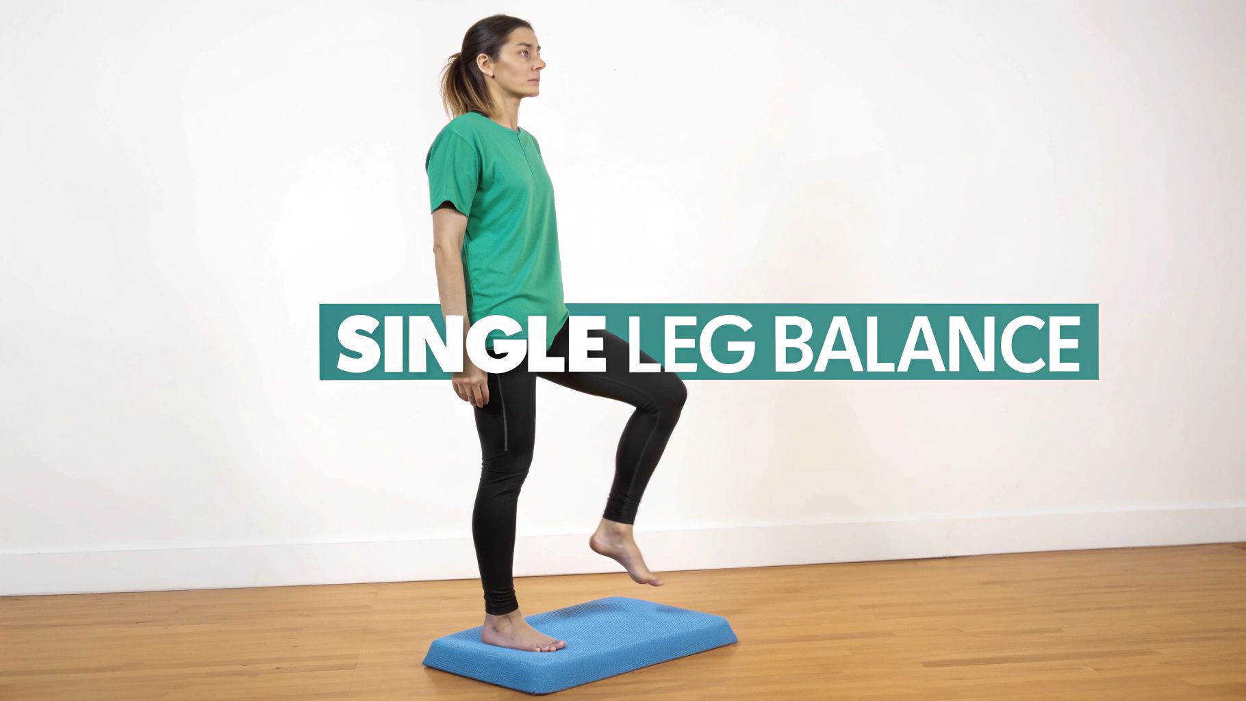 A woman in a green shirt performs a single leg balance exercise on a blue pad.