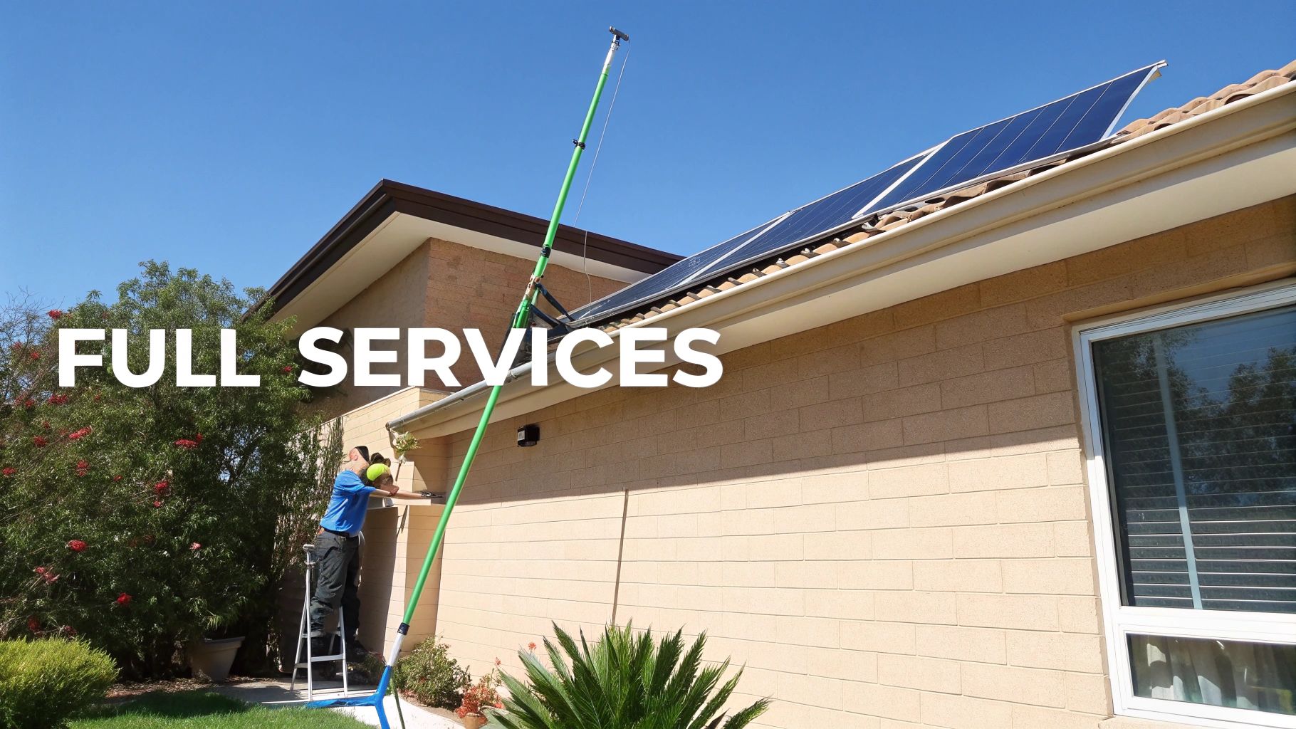 A worker on a ladder cleans a residential house gutter with a long pole, near solar panels.