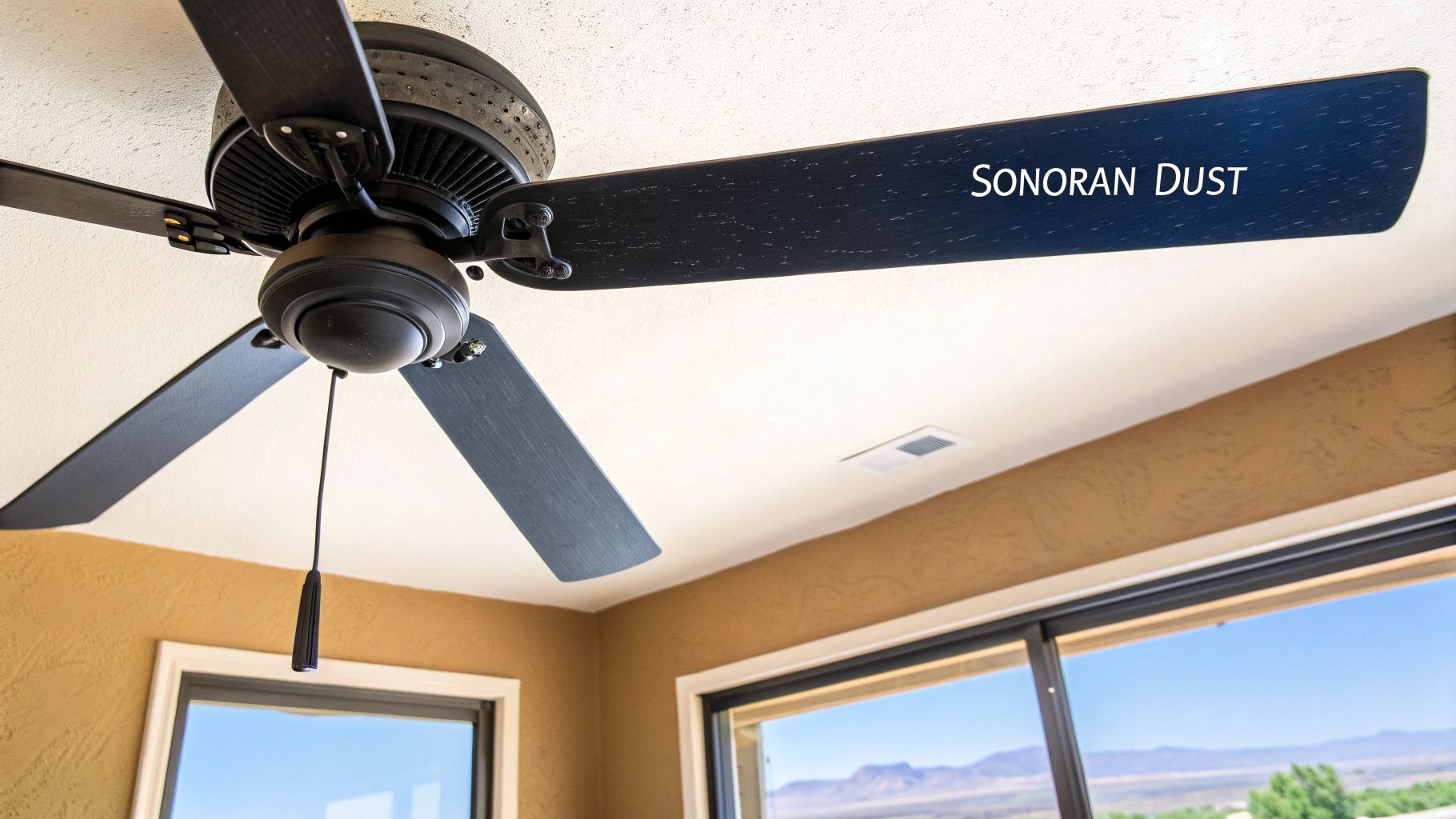 Modern black ceiling fan featuring 'SONORAN DUST' text, mounted on a textured white ceiling.