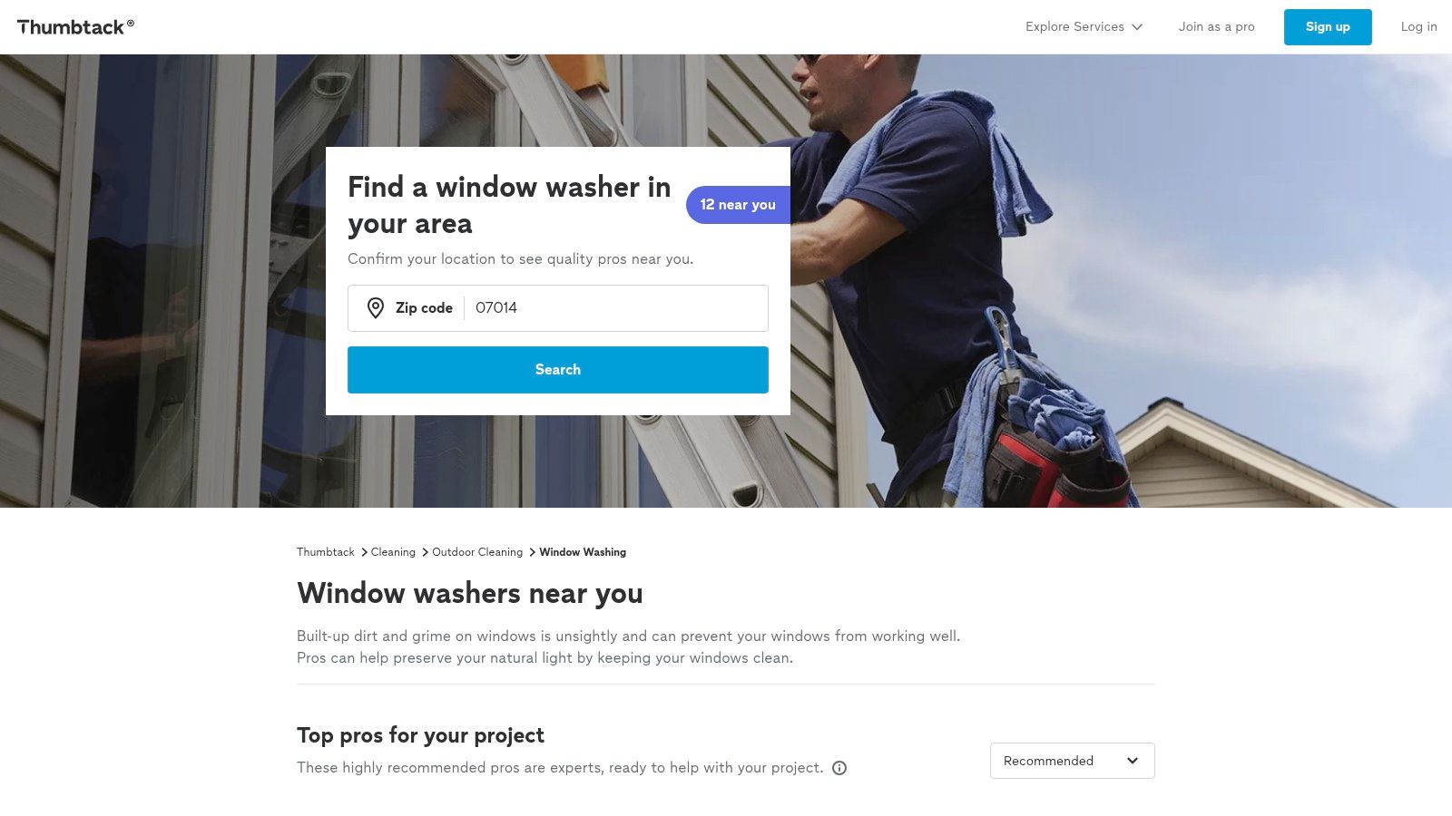A professional window washer uses a squeegee on a large commercial window, showcasing the kind of services found on Thumbtack.