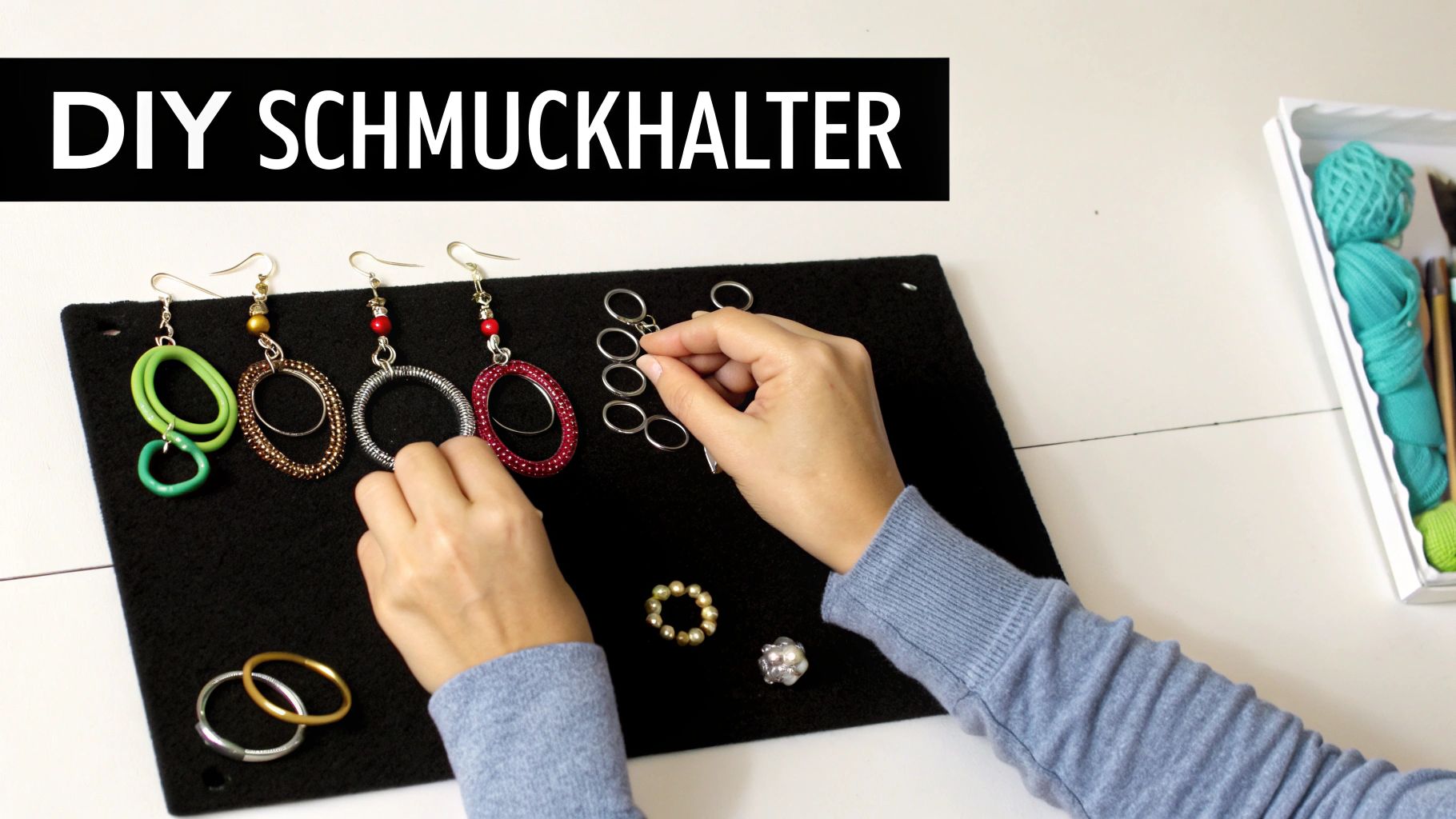Hände ordnen Ohrringe und Ringe auf einem schwarzen DIY Schmuckhalter an.