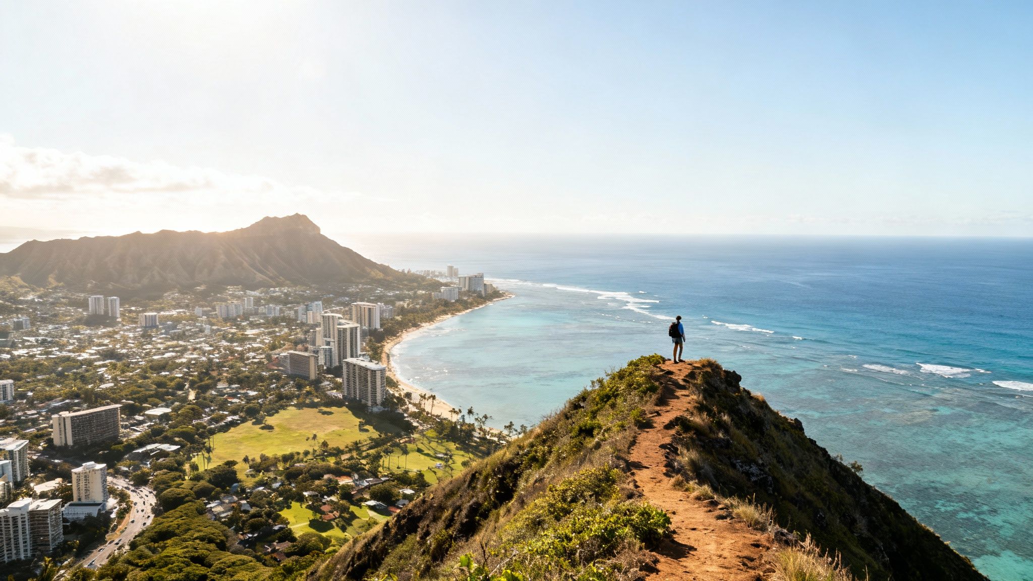 Hiker on a mountain ridge overlooking Waikiki city, beach, ocean, and Diamond Head volcano.