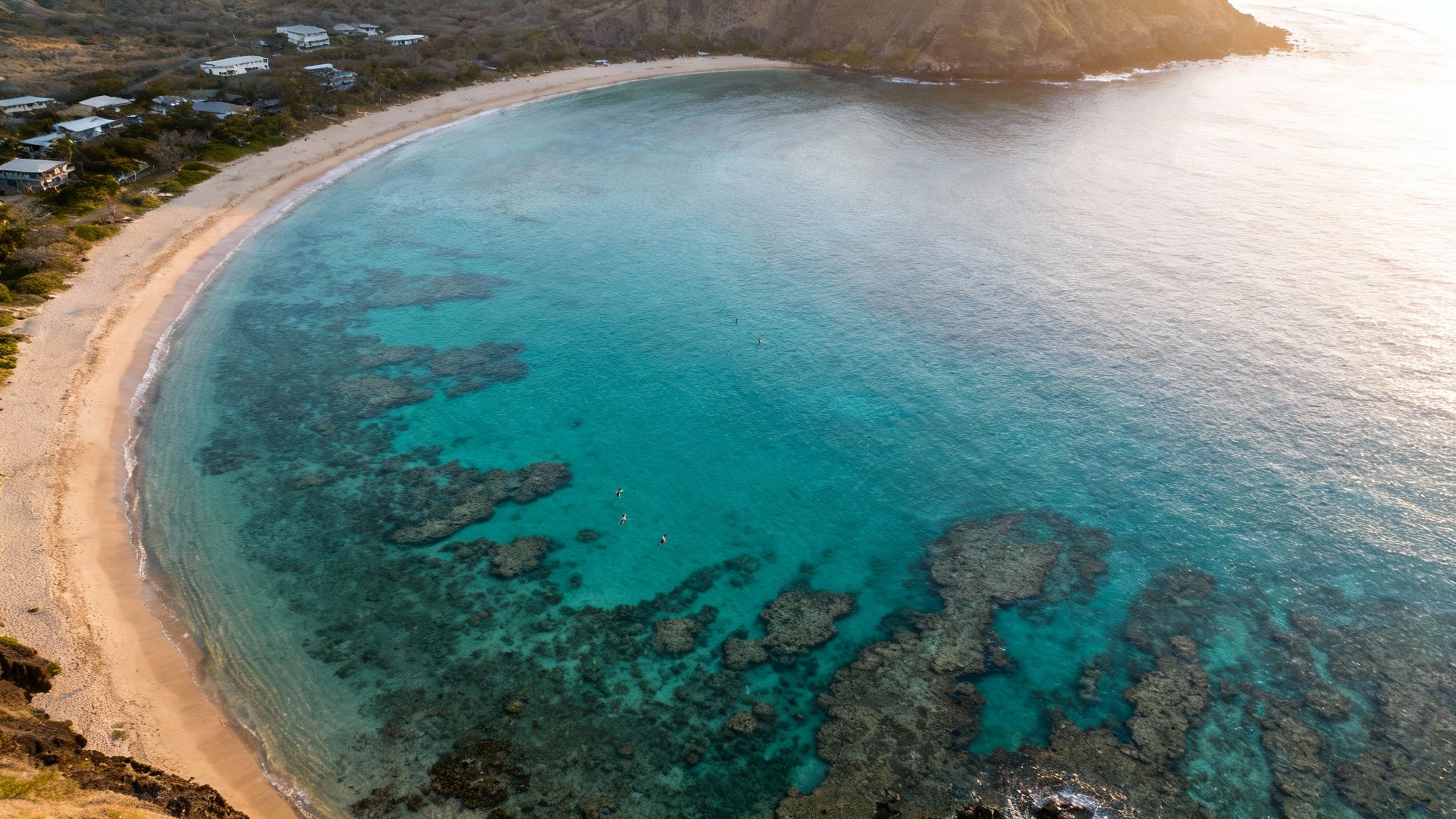 Aerial view of a stunning tropical bay with clear turquoise water, sandy beach, and visible coral reefs.