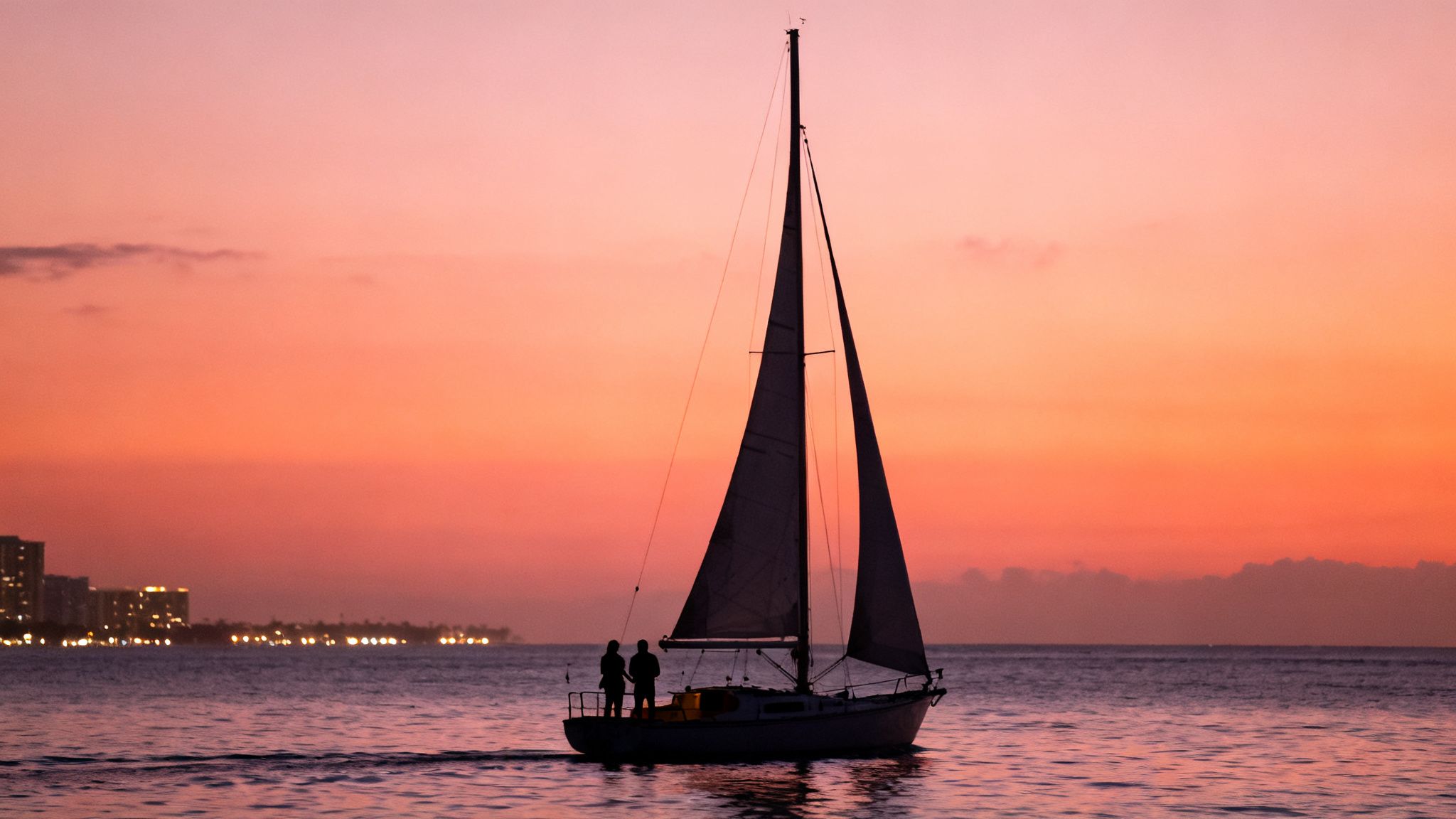 A silhouette of a sailboat with two people on board sailing into a vibrant sunset over the ocean.