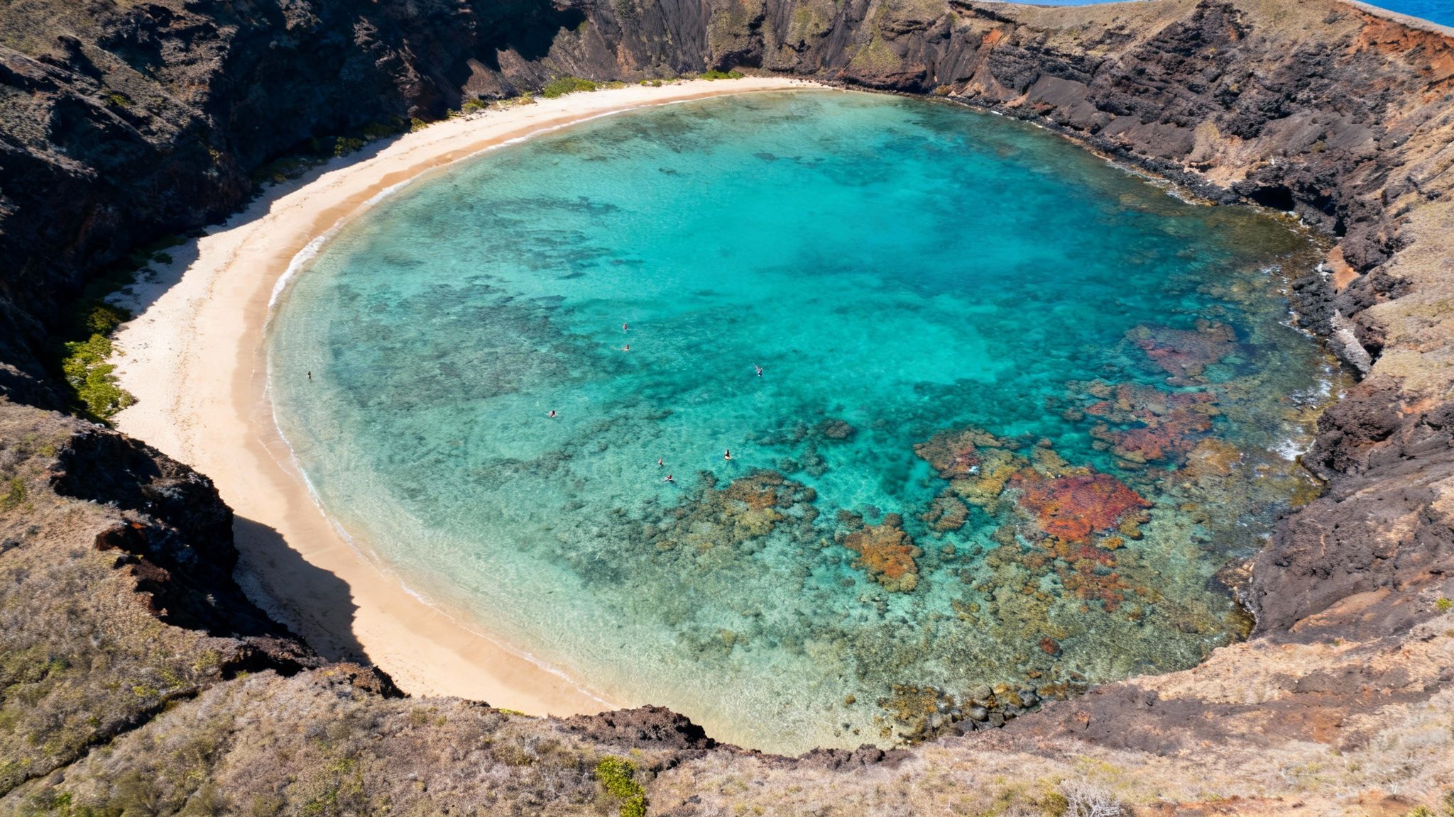 Aerial view of a picturesque volcanic crater bay with a sandy beach and clear turquoise water.