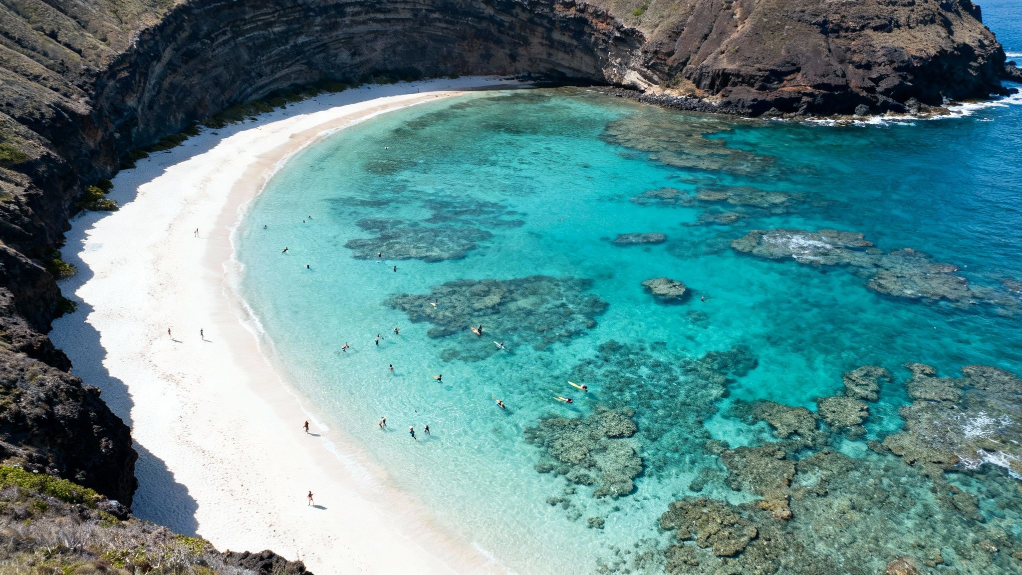 Aerial view of a beautiful Hawaiian beach with people snorkeling in clear turquoise waters.