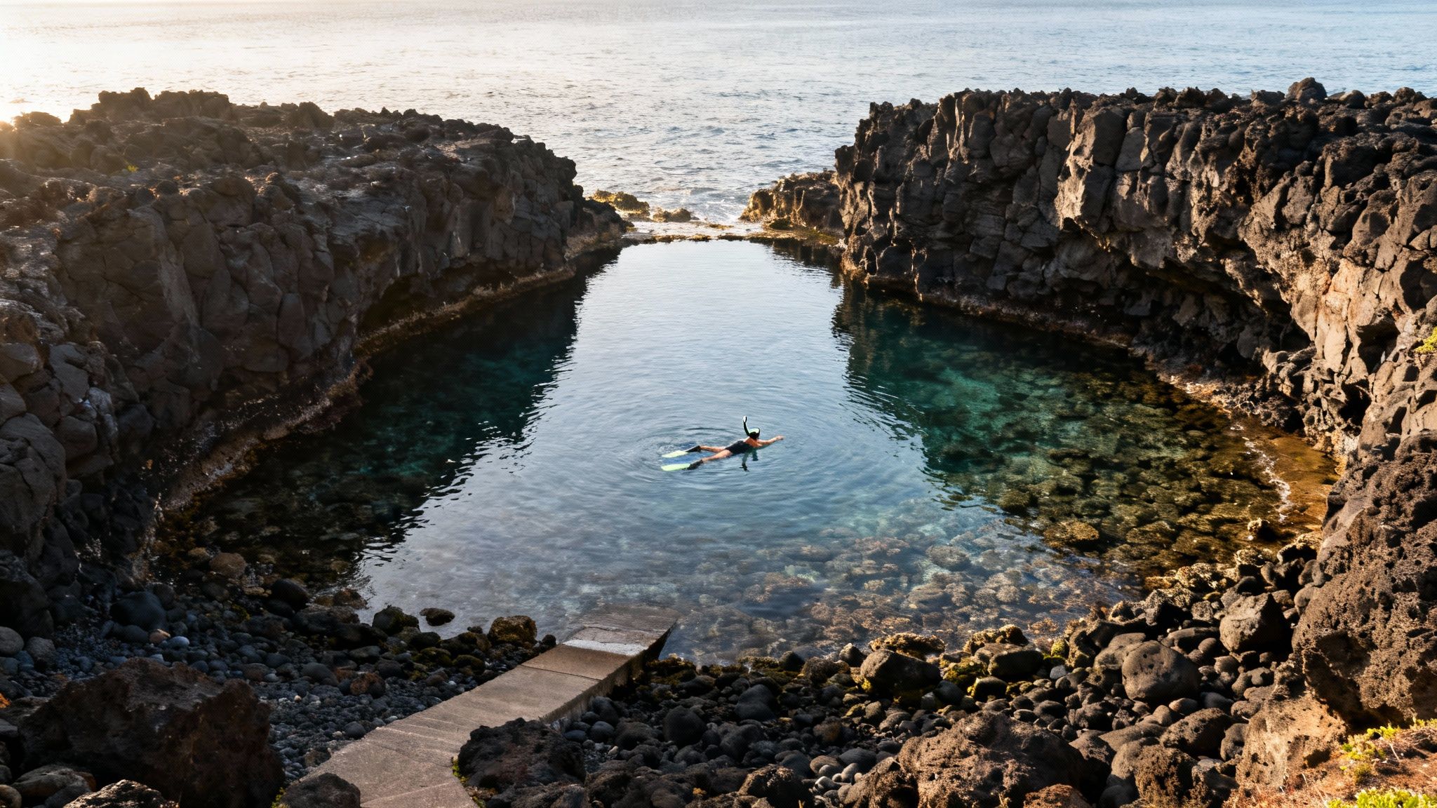 A person snorkeling in a clear natural pool surrounded by dark volcanic rocks, with the ocean in the background.