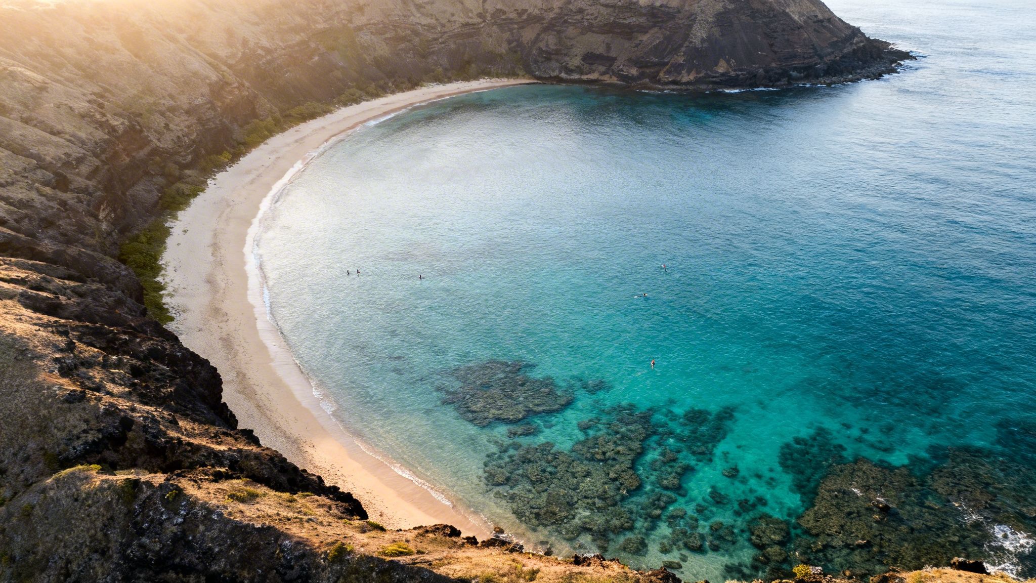 Aerial view of a stunning tropical bay with clear turquoise water, sandy beach, and rocky cliffs.