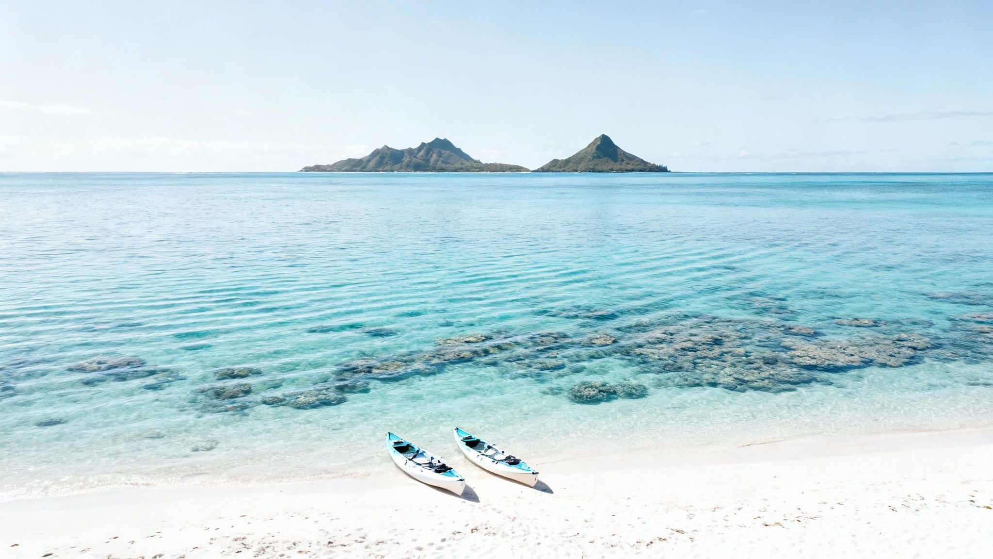 Two kayaks on a pristine white sand beach, facing clear turquoise ocean with distant tropical islands.