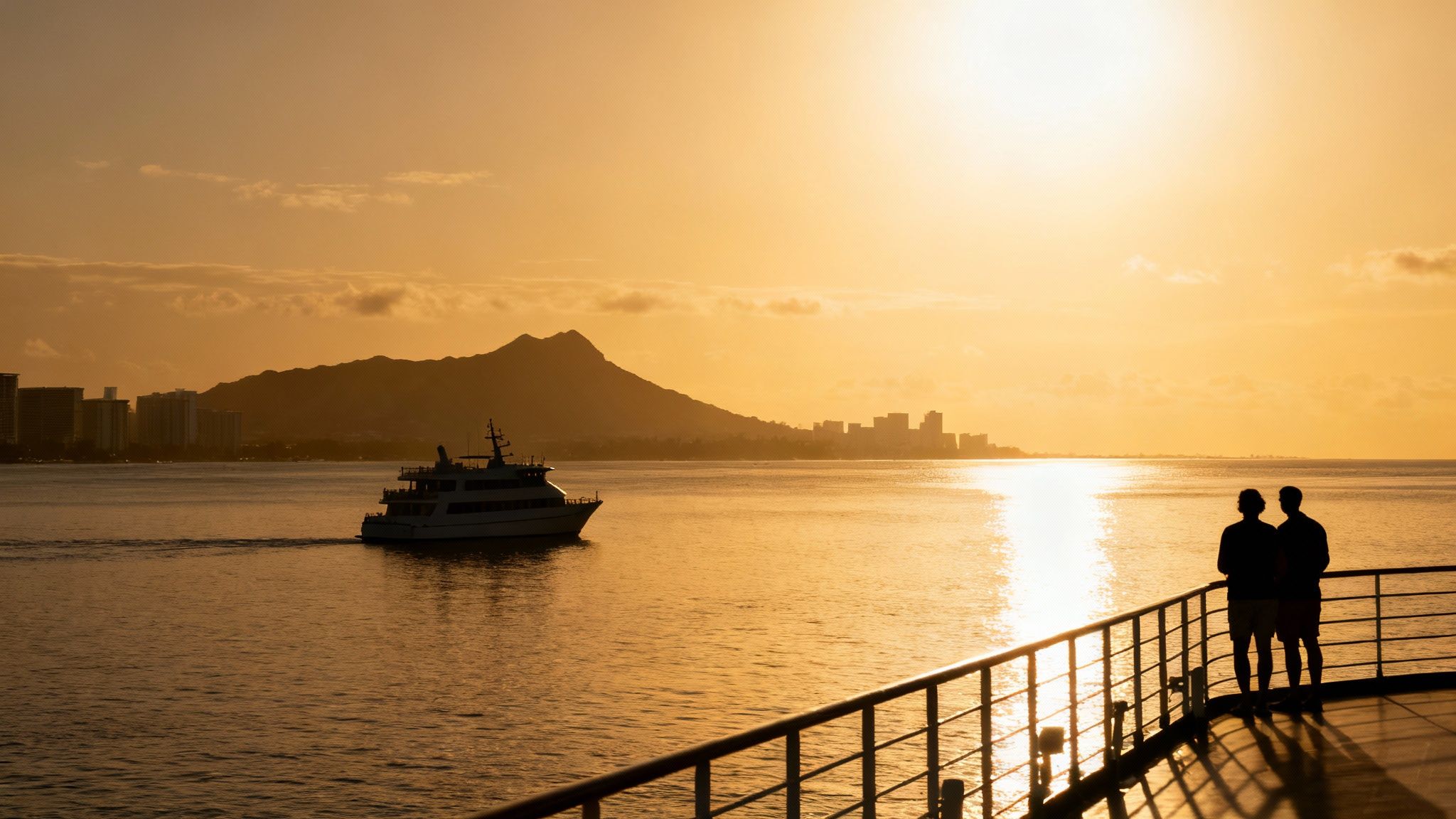 Silhouetted couple watches a golden sunset over the ocean with a boat, mountains, and Honolulu skyline.