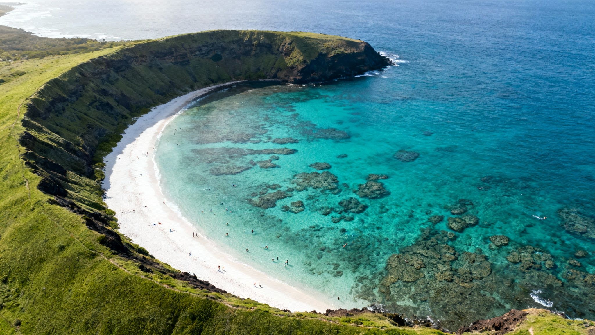 Aerial view of a stunning crescent beach with turquoise water, coral reefs, and people snorkeling.