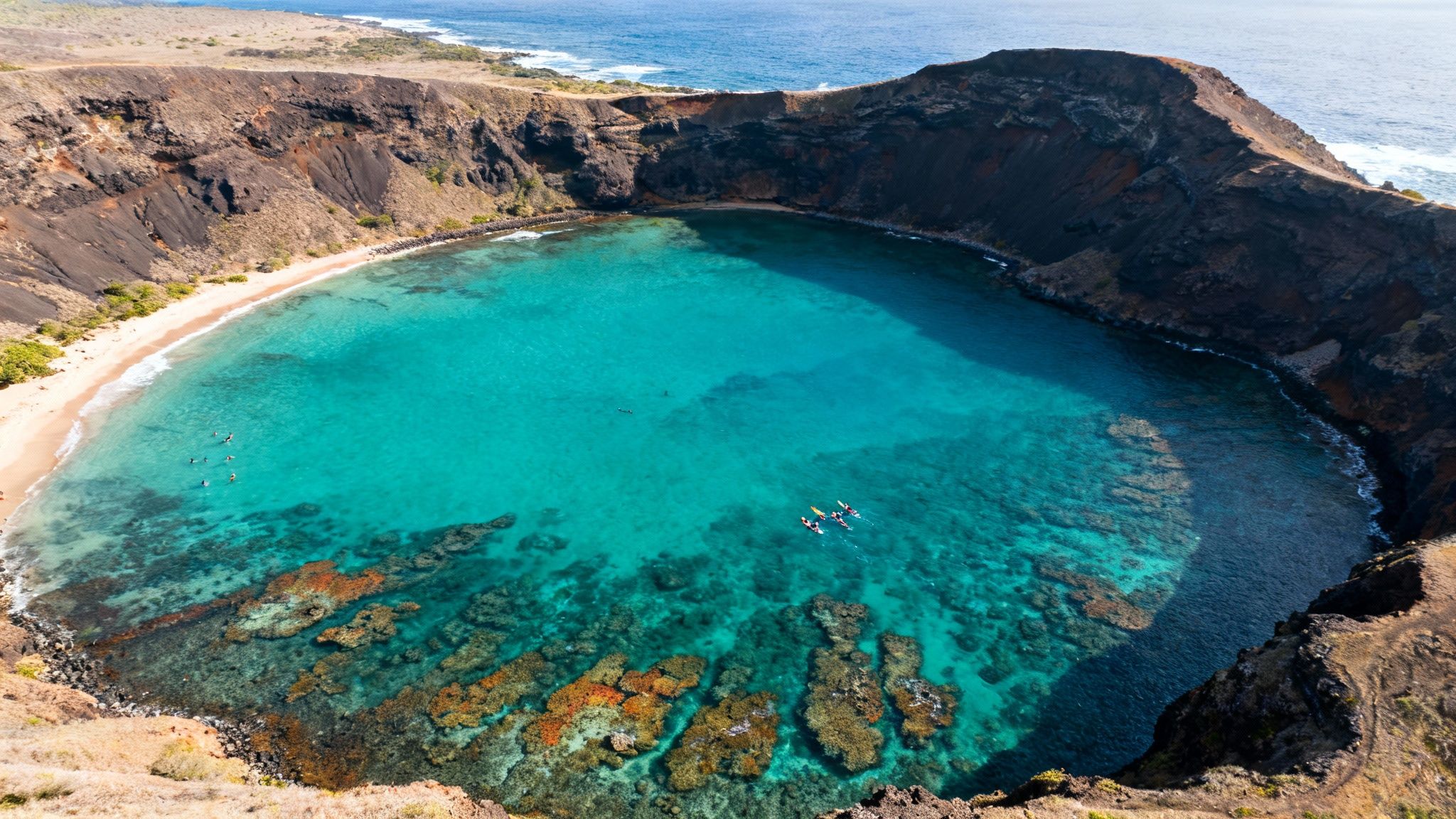 Aerial view of a stunning turquoise bay inside a volcanic crater with people snorkeling and kayaking.