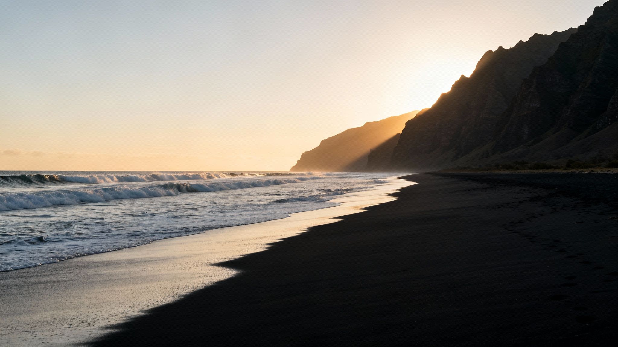 Dramatic sunset over a black sand beach with crashing waves and towering cliffs.