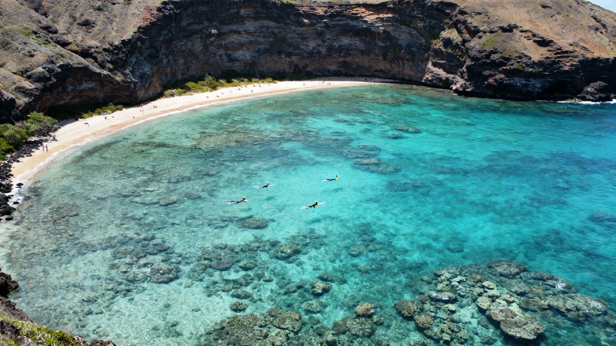 Aerial view of a stunning tropical bay with snorkelers in clear turquoise water and a sandy beach.
