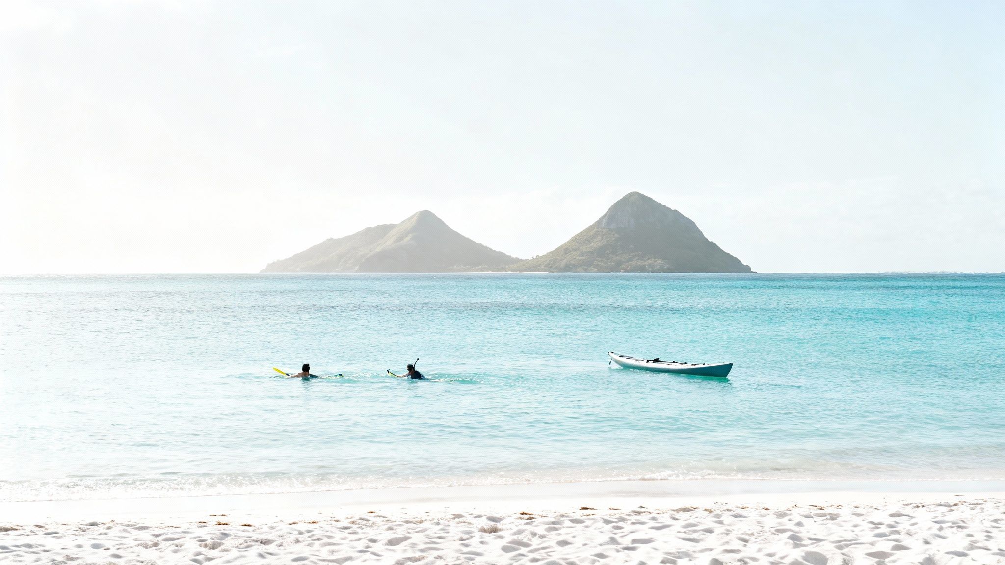 Two people snorkeling near a white kayak off a tropical beach with two islands in the background.