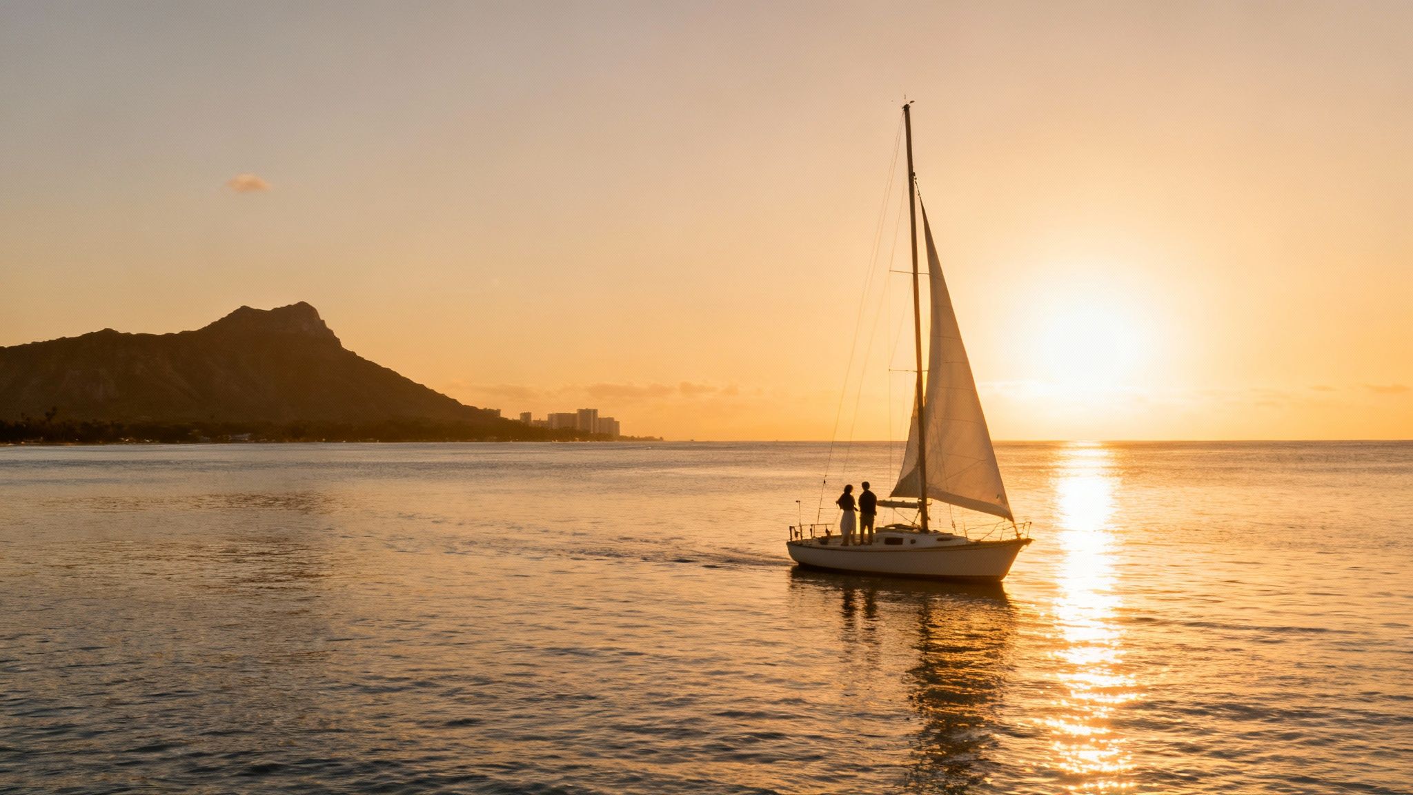 Silhouette of a couple on a sailboat during a golden sunset, with Diamond Head mountain.