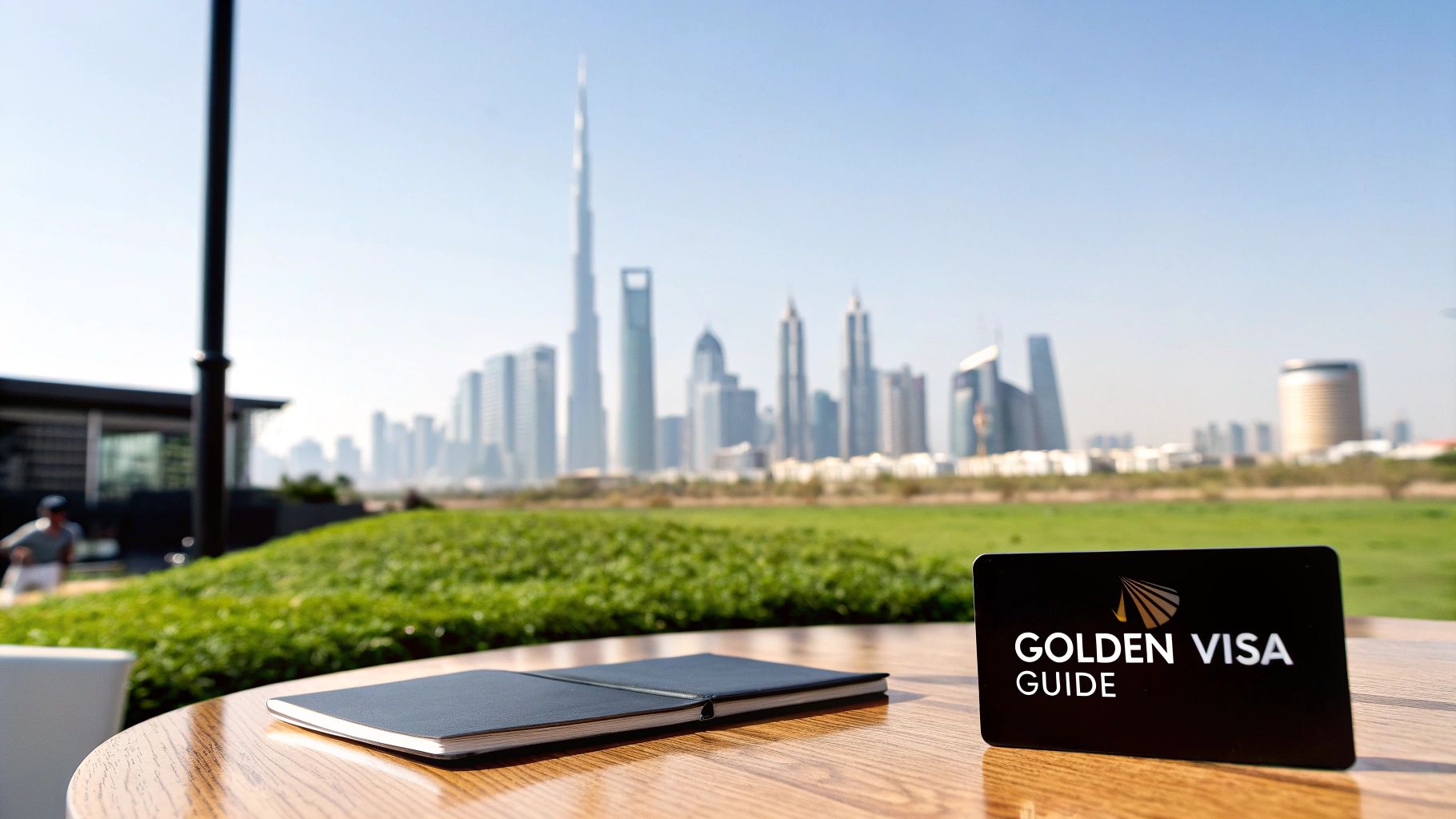 A 'Golden Visa Guide' card and a notebook on a table, with the iconic Dubai skyline and Burj Khalifa in the background.