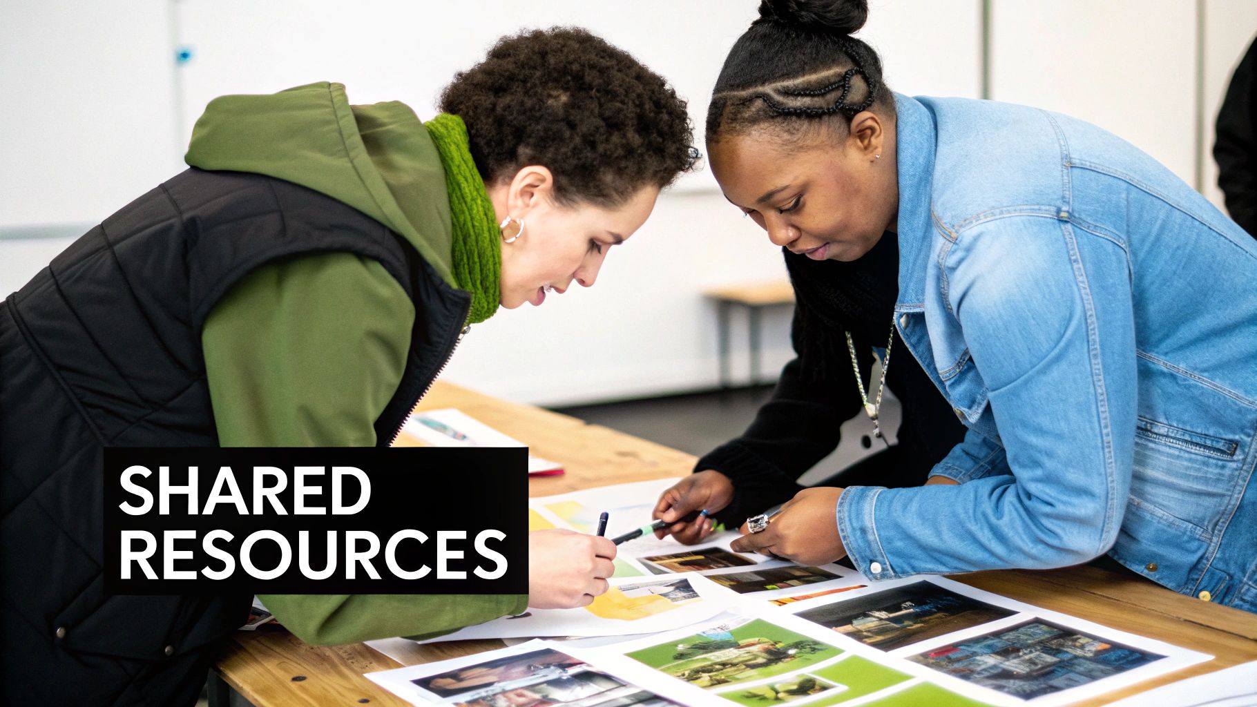 Two women collaborate, leaning over a table to review printed images, symbolizing shared resources.