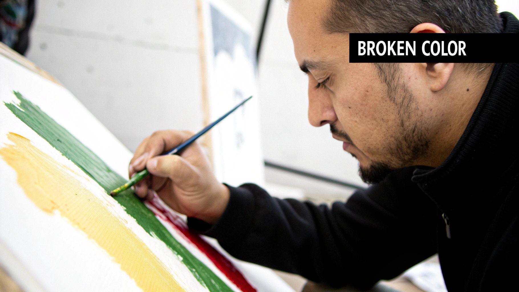 Man with a beard intently painting colorful stripes with a brush on a white canvas.