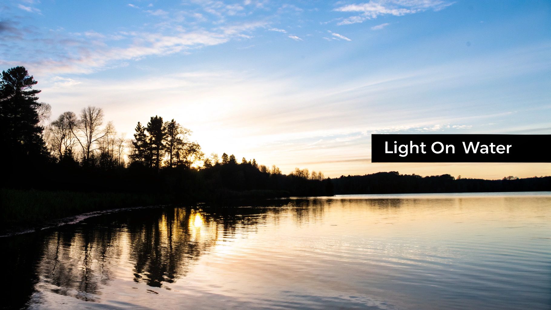 A scenic view of a sunset over a calm lake, with silhouetted trees and golden light reflecting on the water.