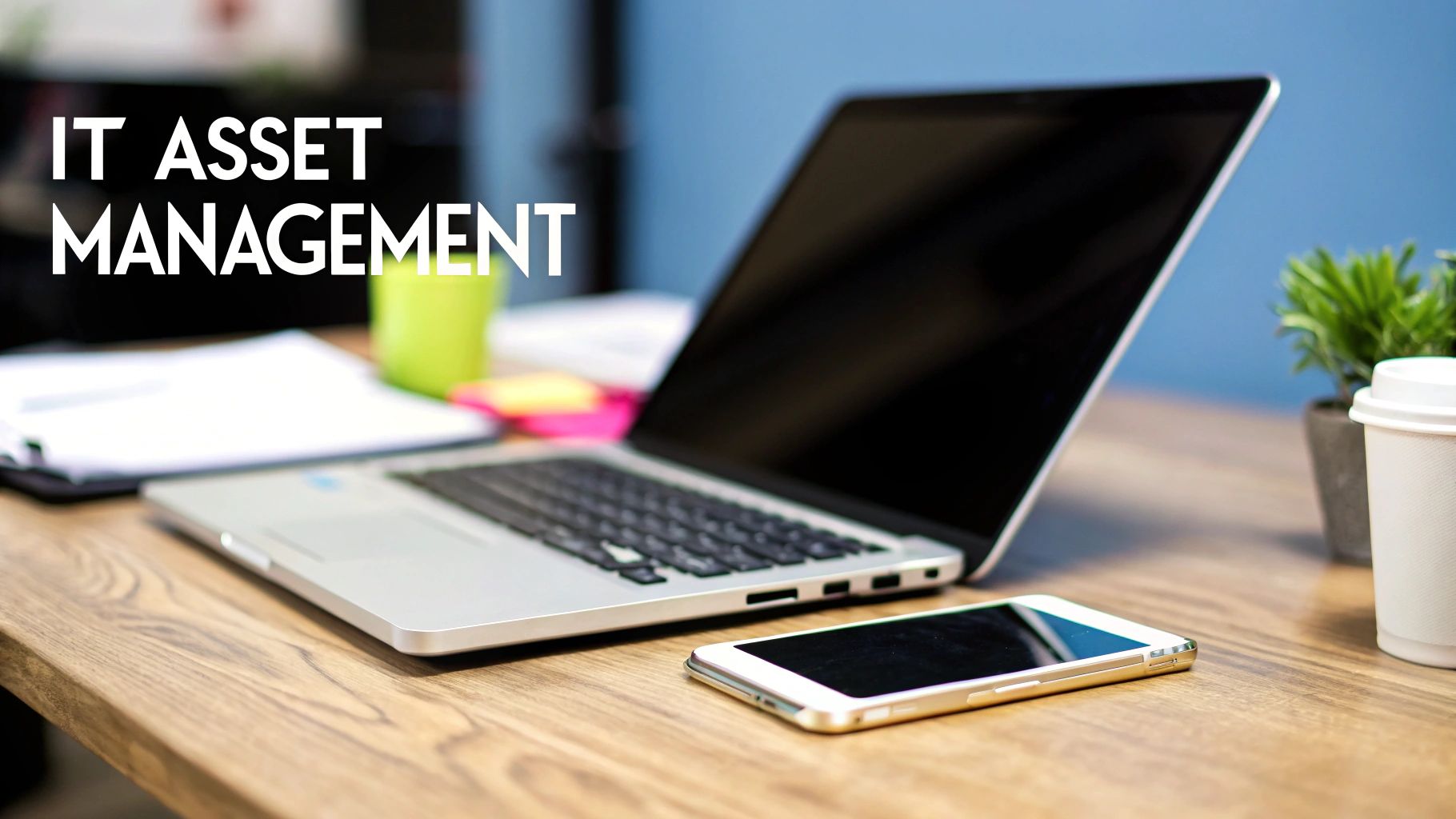 A desk with a laptop, smartphone, documents, and 'IT ASSET MANAGEMENT' text overlaid.