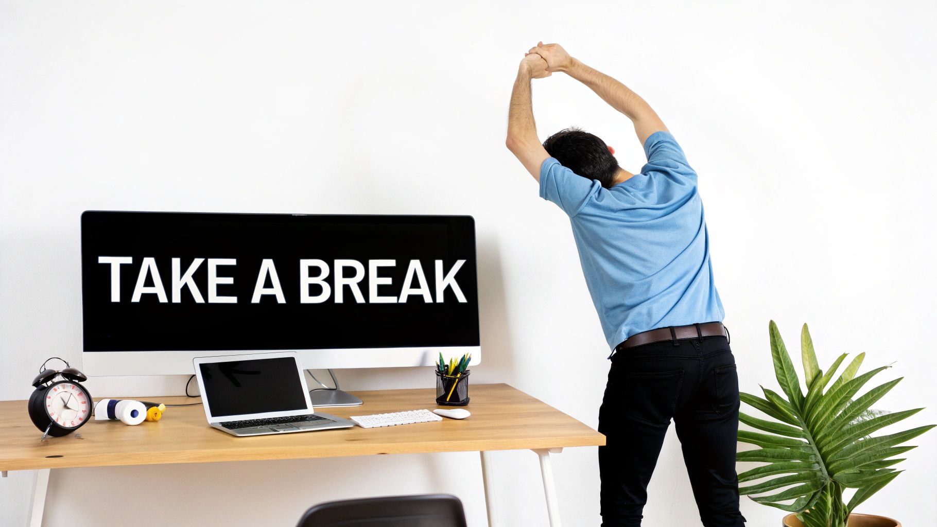 A man stretches his arms above his head at a desk with a monitor displaying 'TAKE A BREAK'.