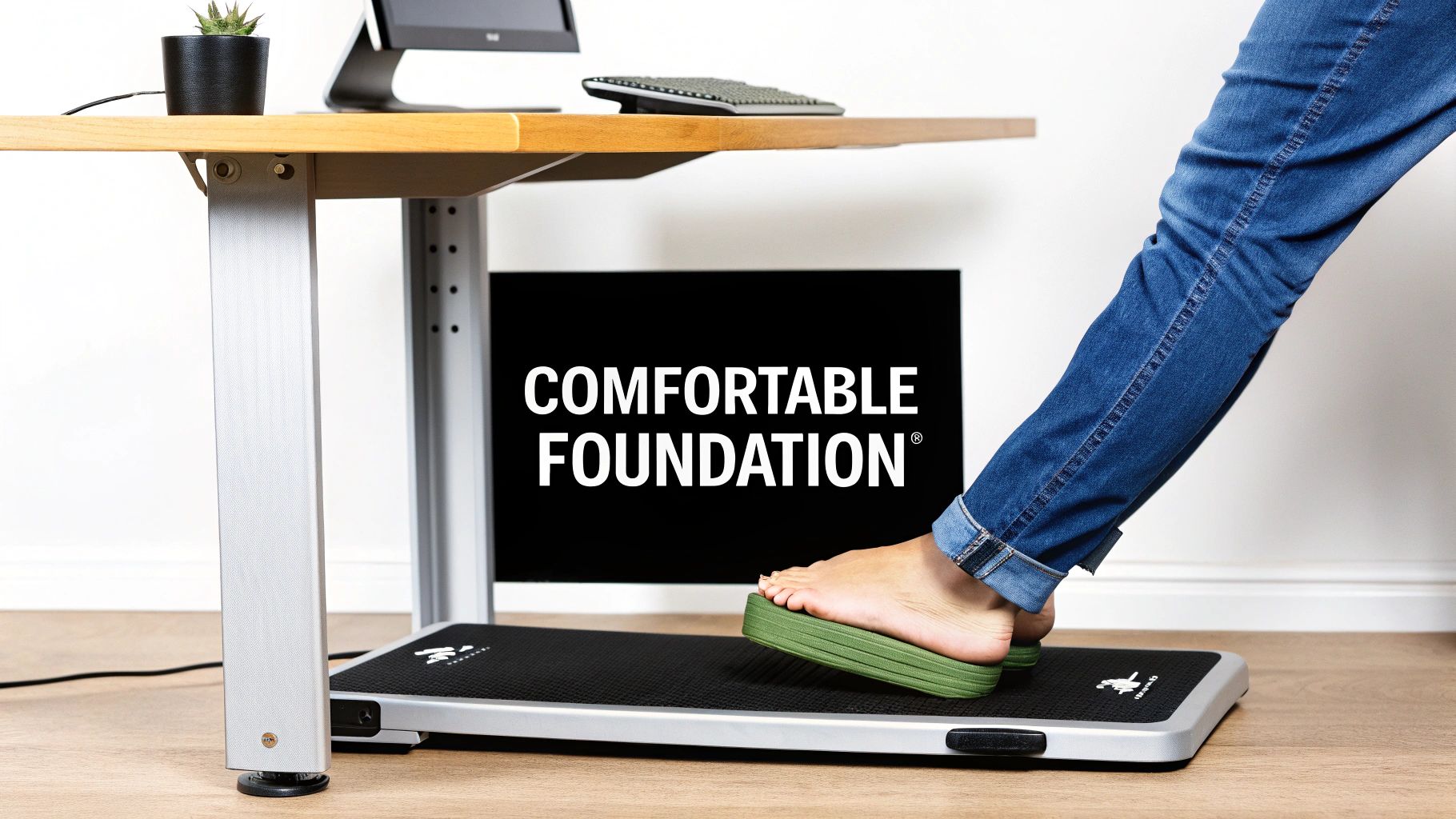 A person's foot on a green footrest on an anti-fatigue mat under a standing desk.