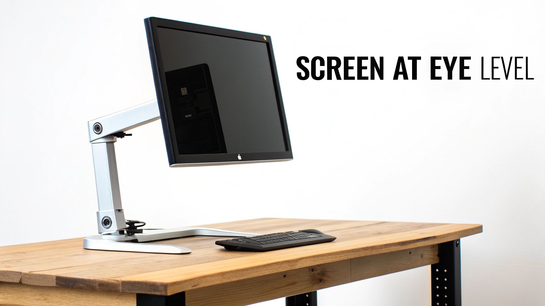 An adjustable monitor stand holding an Apple display at eye level on a wooden desk with a keyboard.