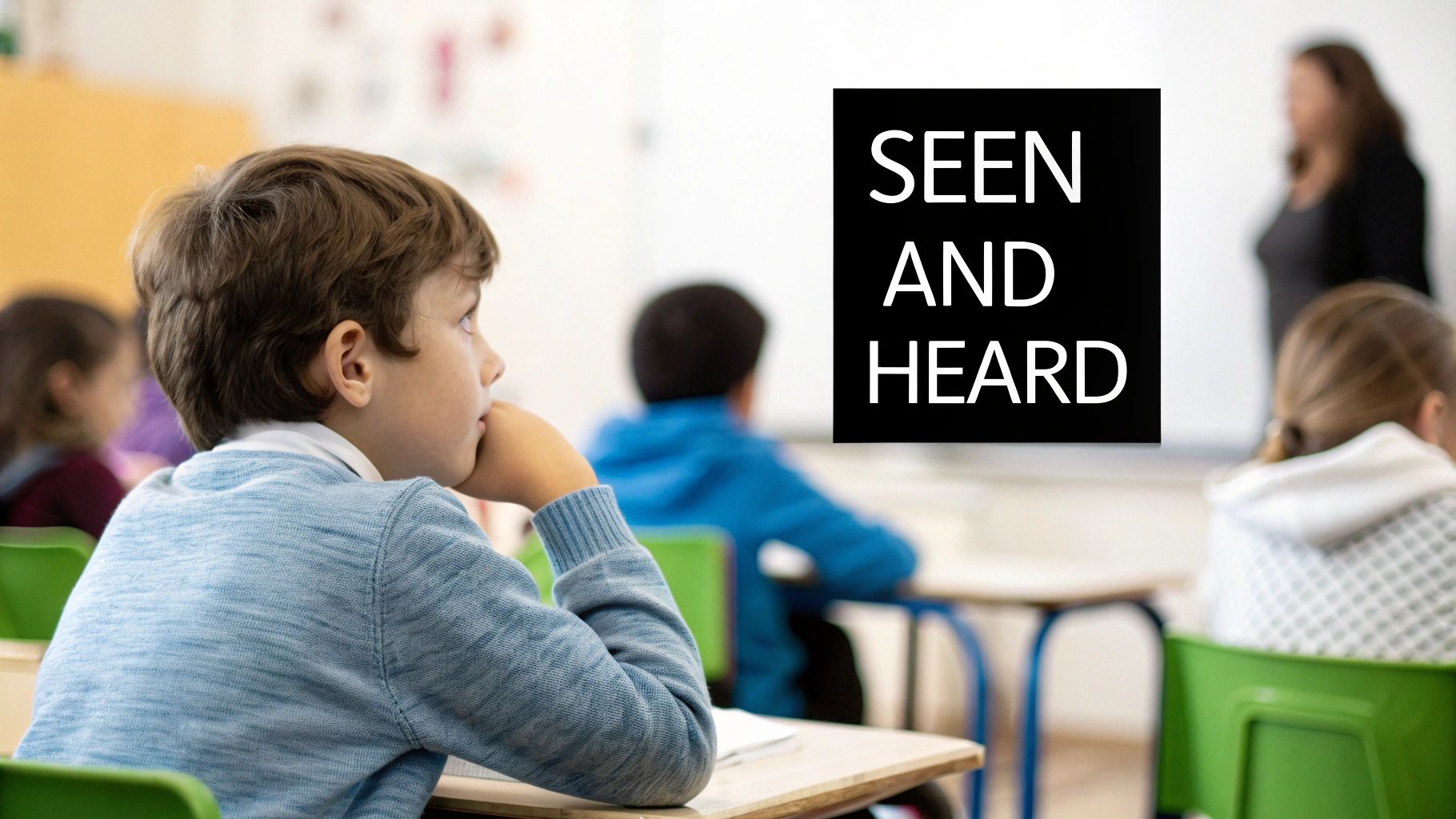 A young boy in a blue sweater attentively watches his teacher in a bright classroom.