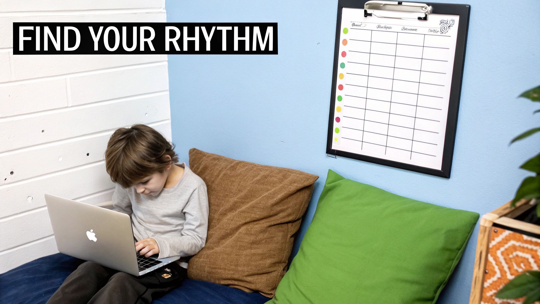 A young boy sits comfortably on a cushion, engrossed in his laptop, with a chore chart on the blue wall.
