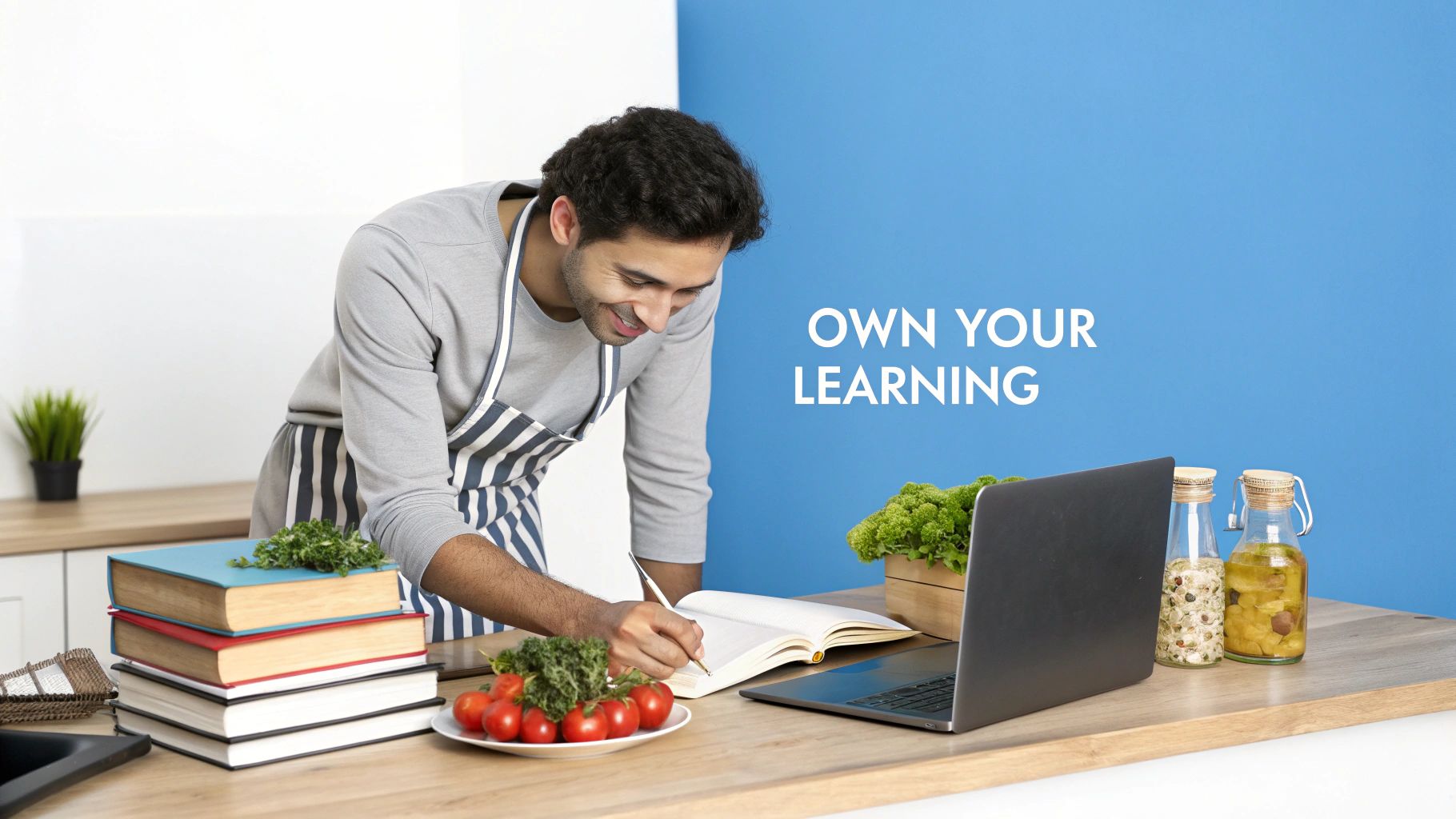 Smiling man in apron writes in a notebook near a laptop, books, and fresh produce.
