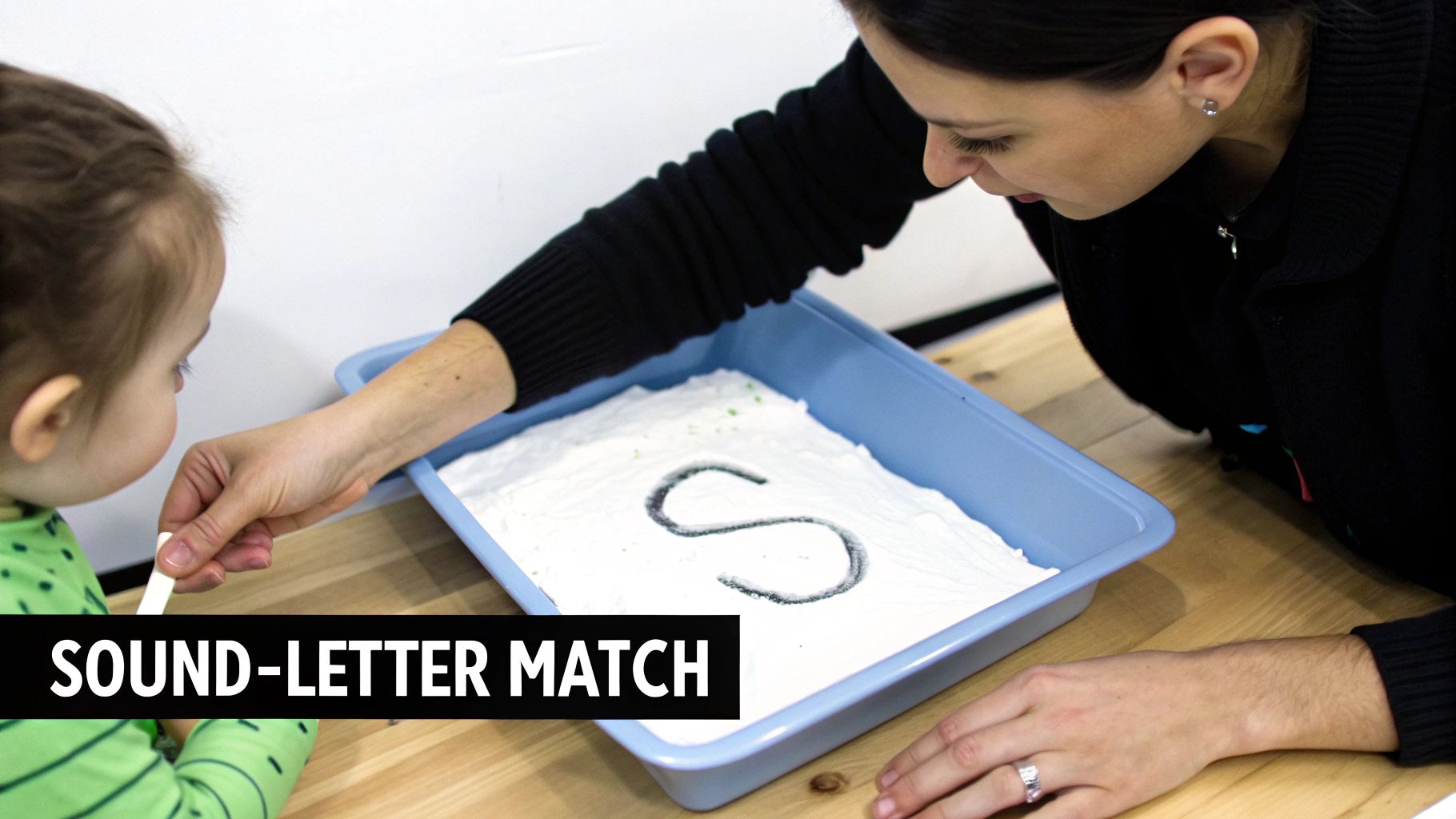 A young child tracing letters in a sand tray, engaging in multi-sensory learning.