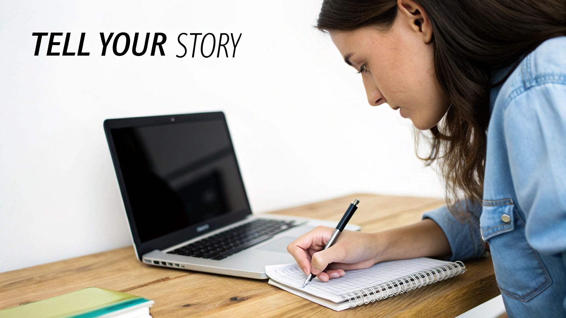 A young woman diligently writing in a notebook, with a laptop beside her and text 'TELL YOUR STORY'.