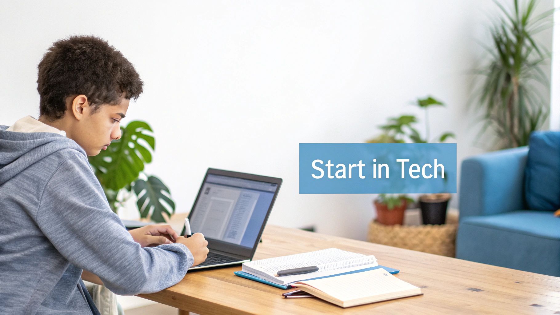 A young person intently using a laptop with a stylus on a wooden desk, with notebooks and a "Start in Tech" banner.