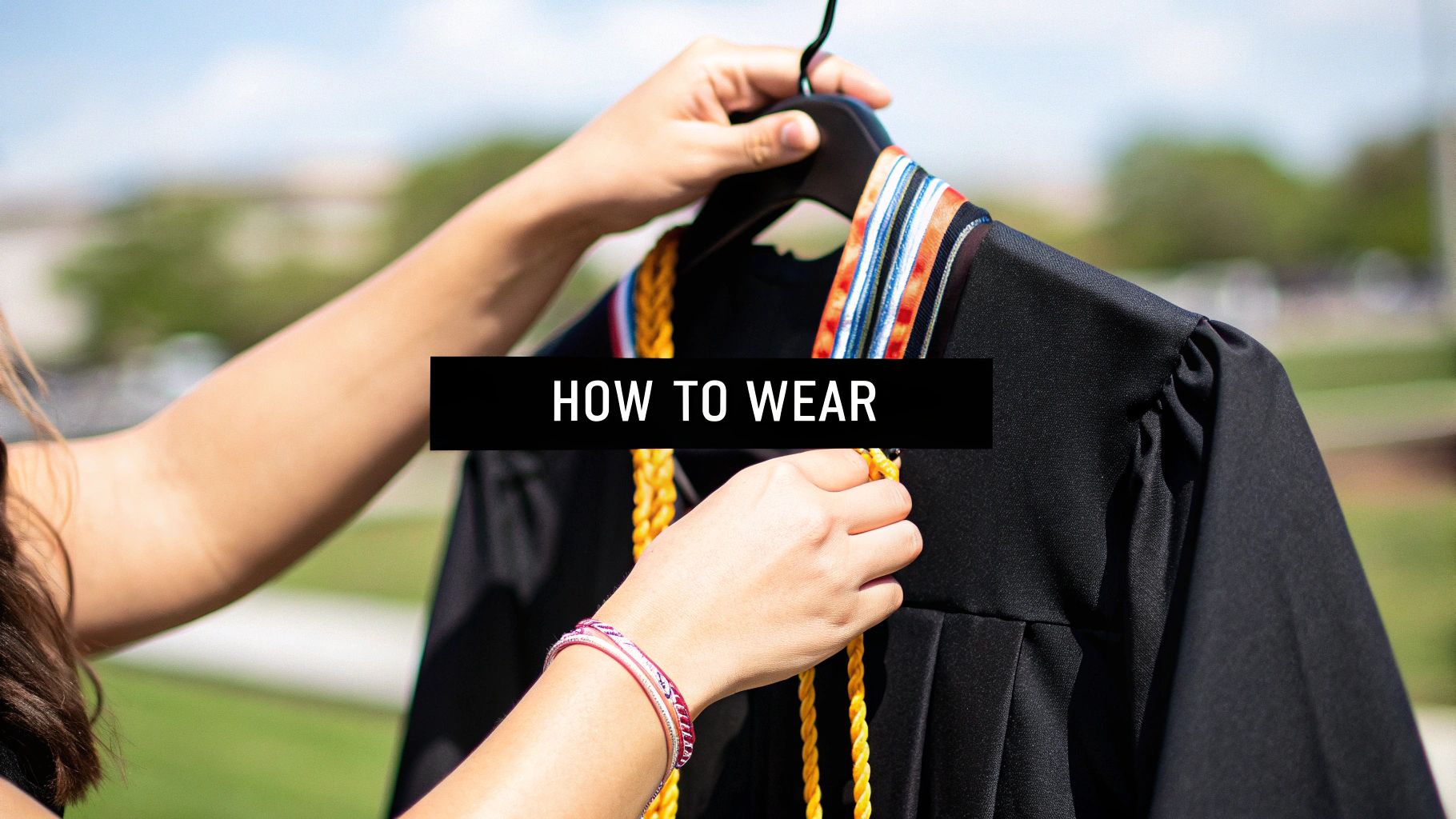 A close-up of hands holding a black graduation gown with colorful stoles and gold honor cords, displaying 'HOW TO WEAR'.