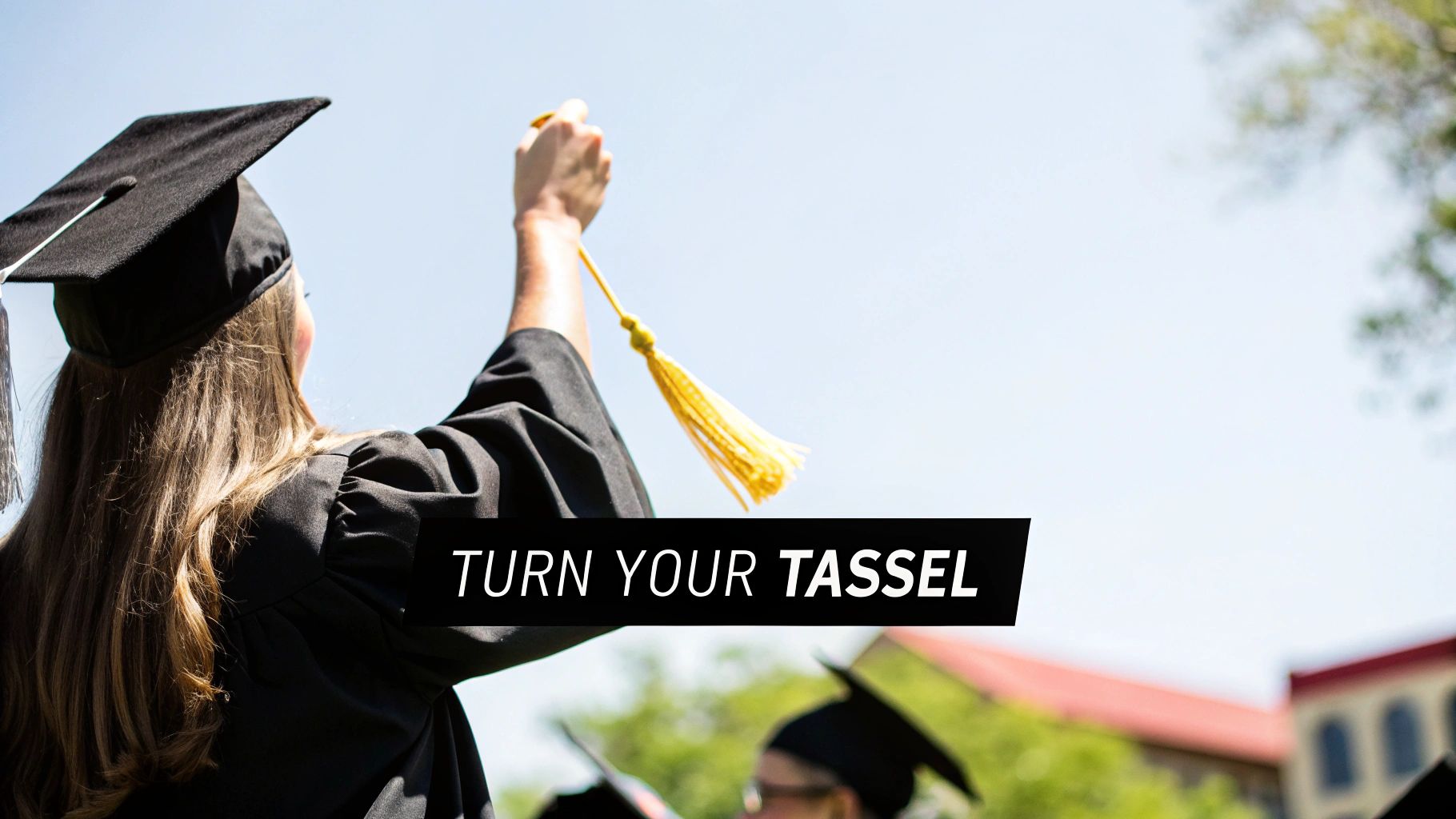 A graduate in a black cap and gown reaches up to turn a yellow tassel against a bright sky.