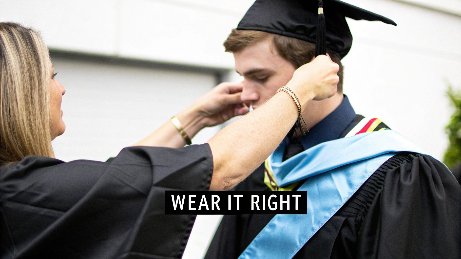 A woman helps a young man adjust his black graduation cap and gown with a light blue stole.