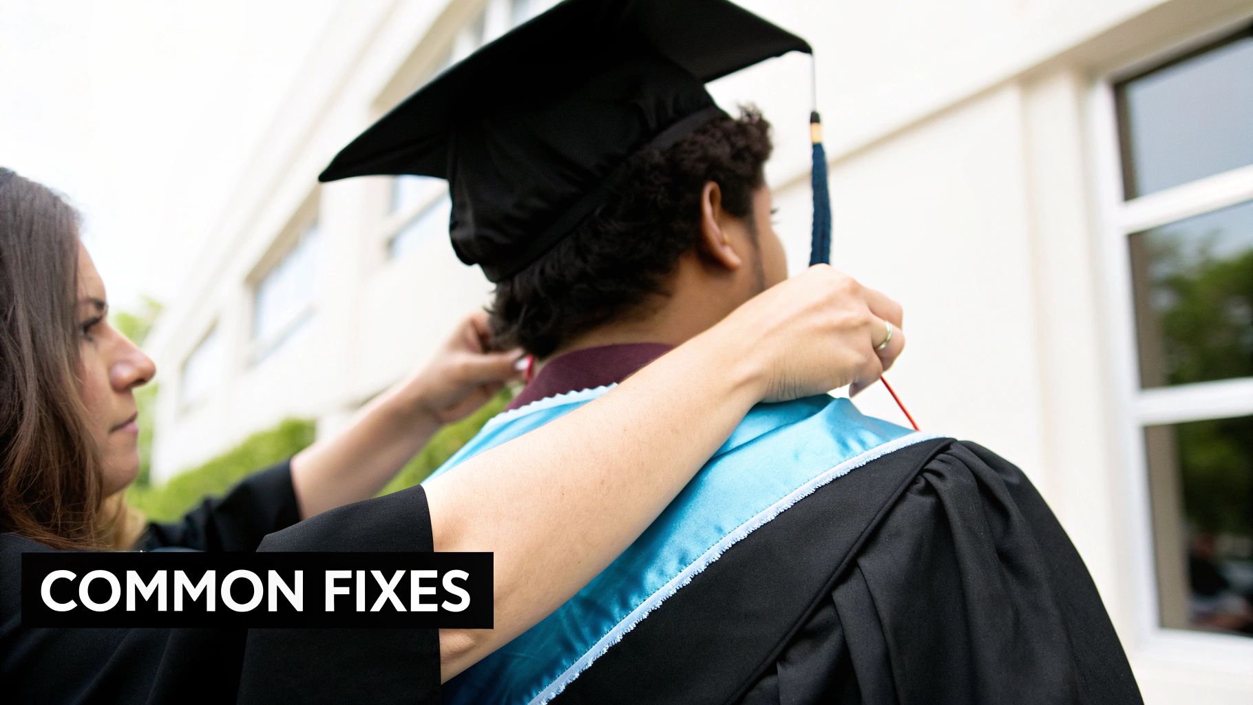 A person helps another student adjust their graduation hood over a cap and gown.