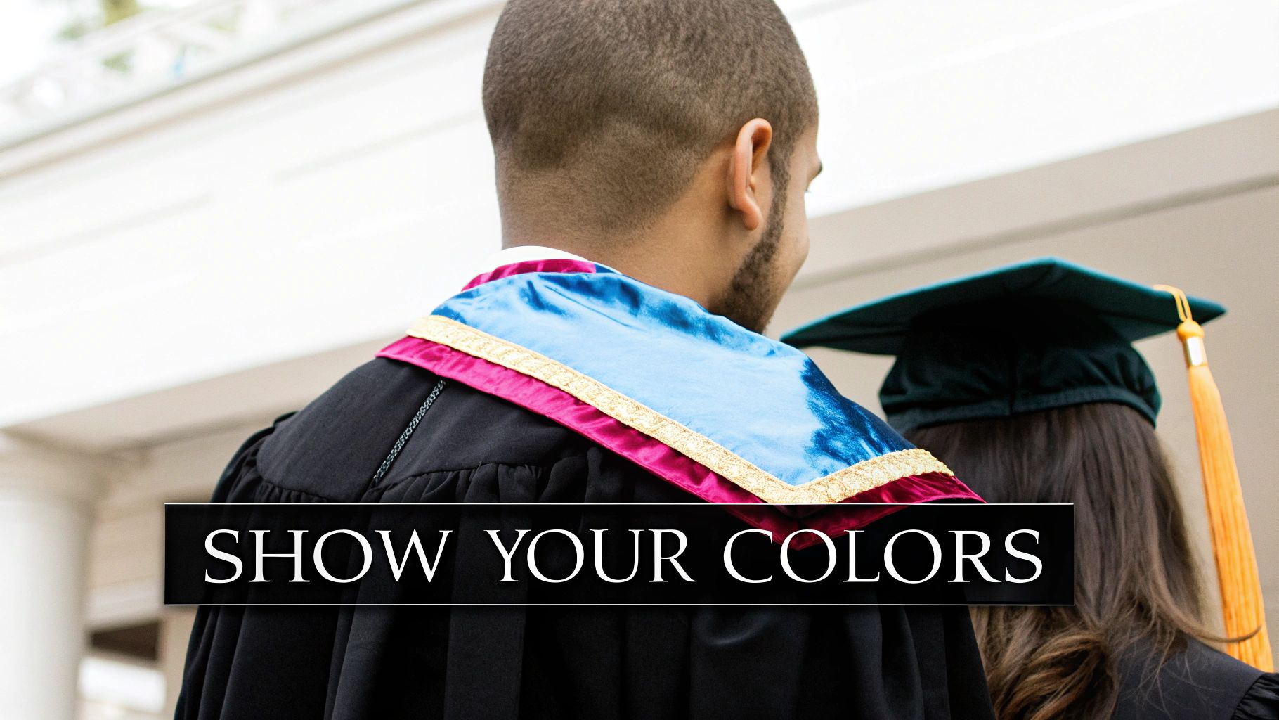 Two graduates from behind, one wearing an academic gown and a colorful hood, celebrating their achievement.
