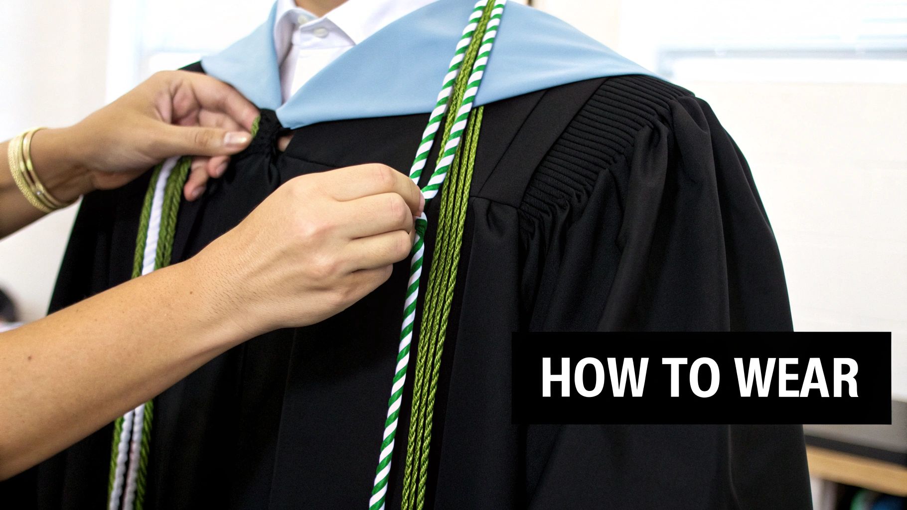 A person's hands adjusting green and white honor cords on a black graduation gown.